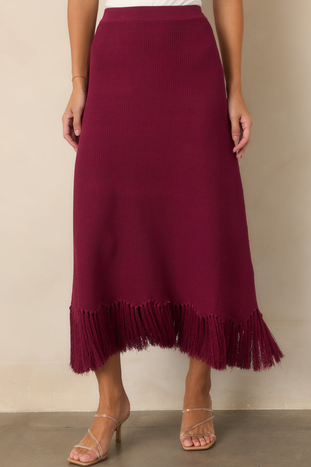 Close-up detail of the rich berry knit texture and fringe-trimmed hem.