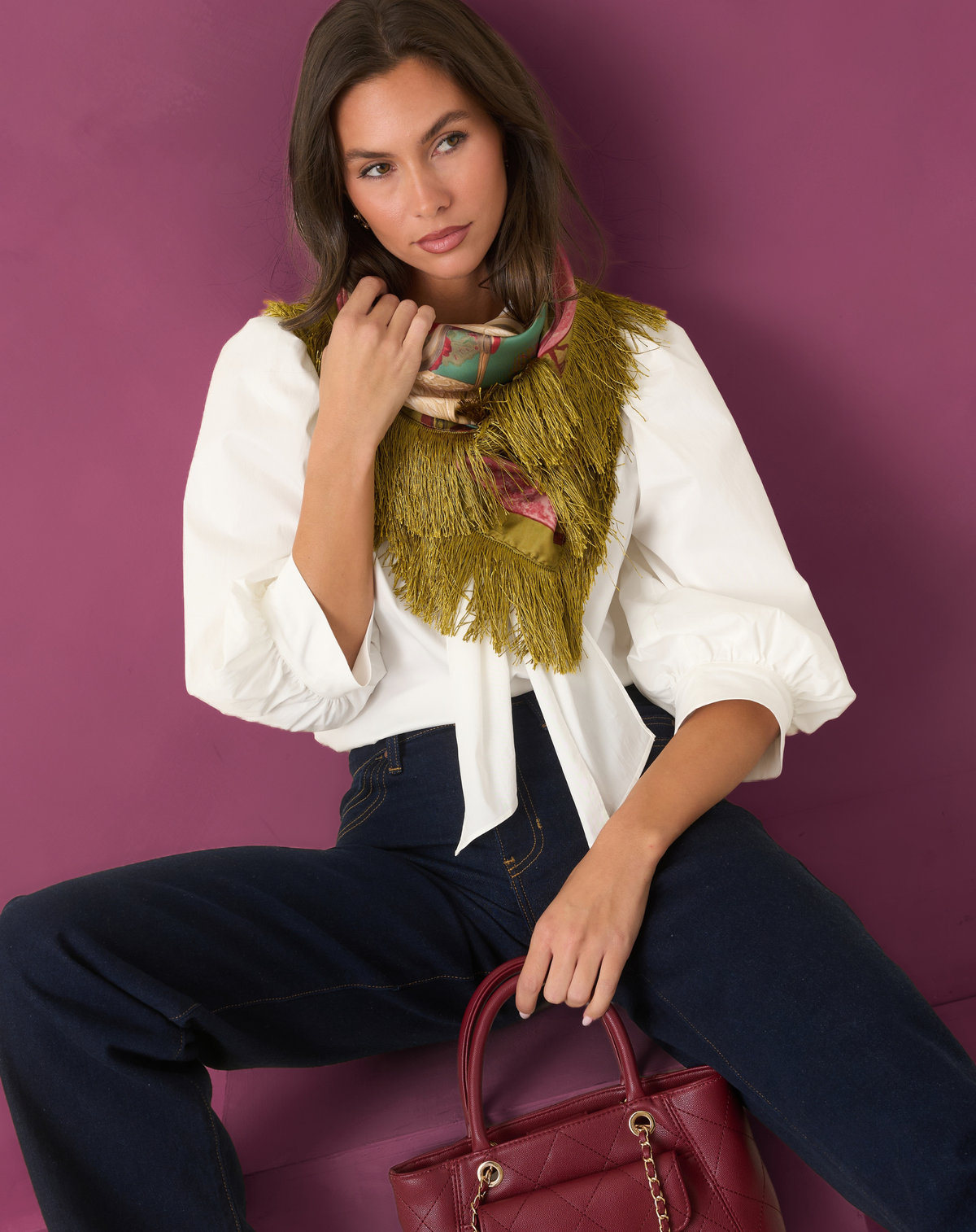 Model wearing a white blouse with a green fringe scarf and dark jeans.