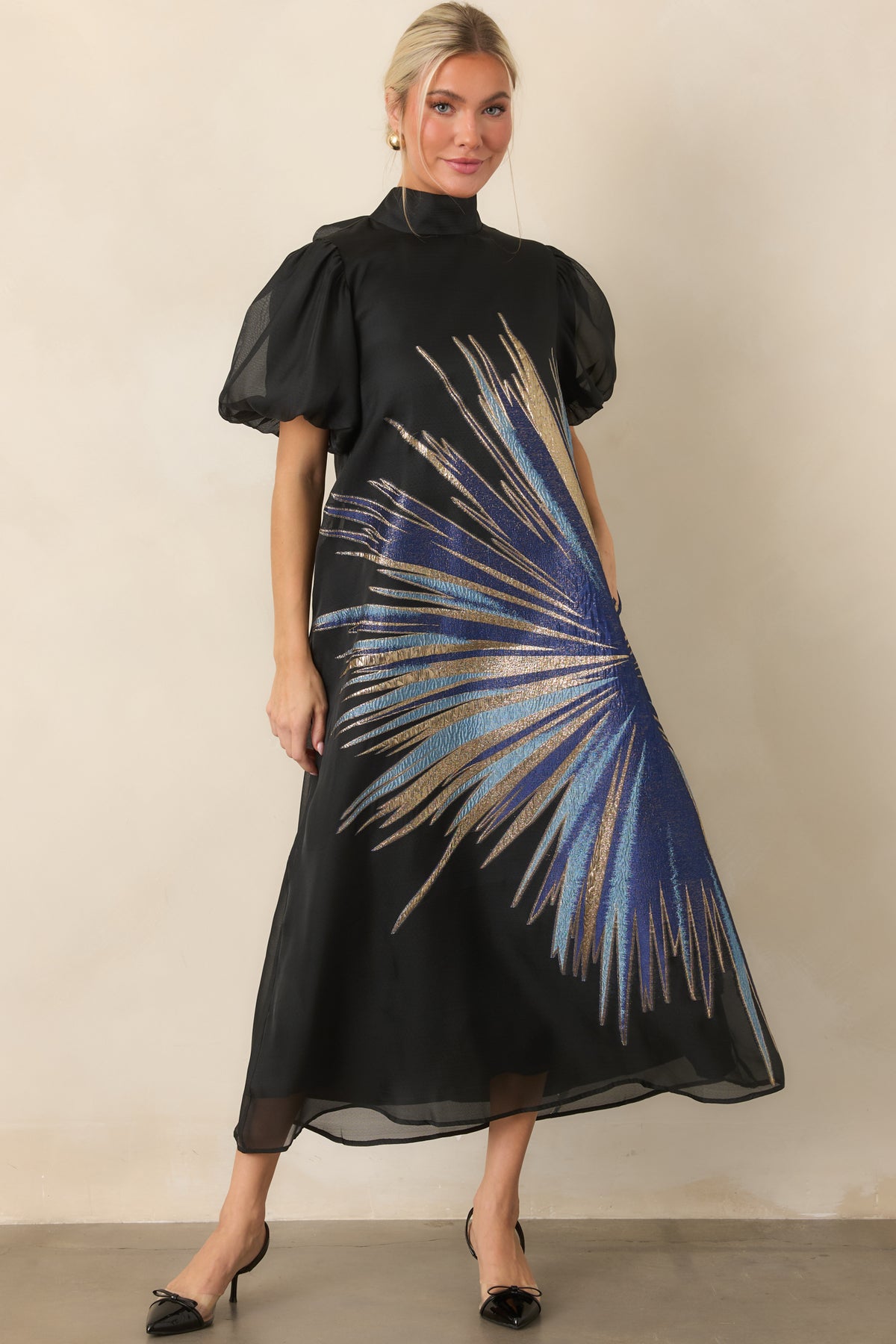 Black A-line midi dress featuring a dramatic metallic starburst pattern, high neckline, and voluminous puff sleeves.