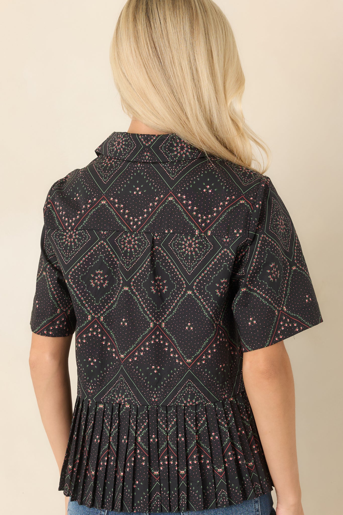 Rear view of the black cotton blouse showcasing the scarf-inspired floral print, short sleeves, and sharply pleated peplum hem for added volume.