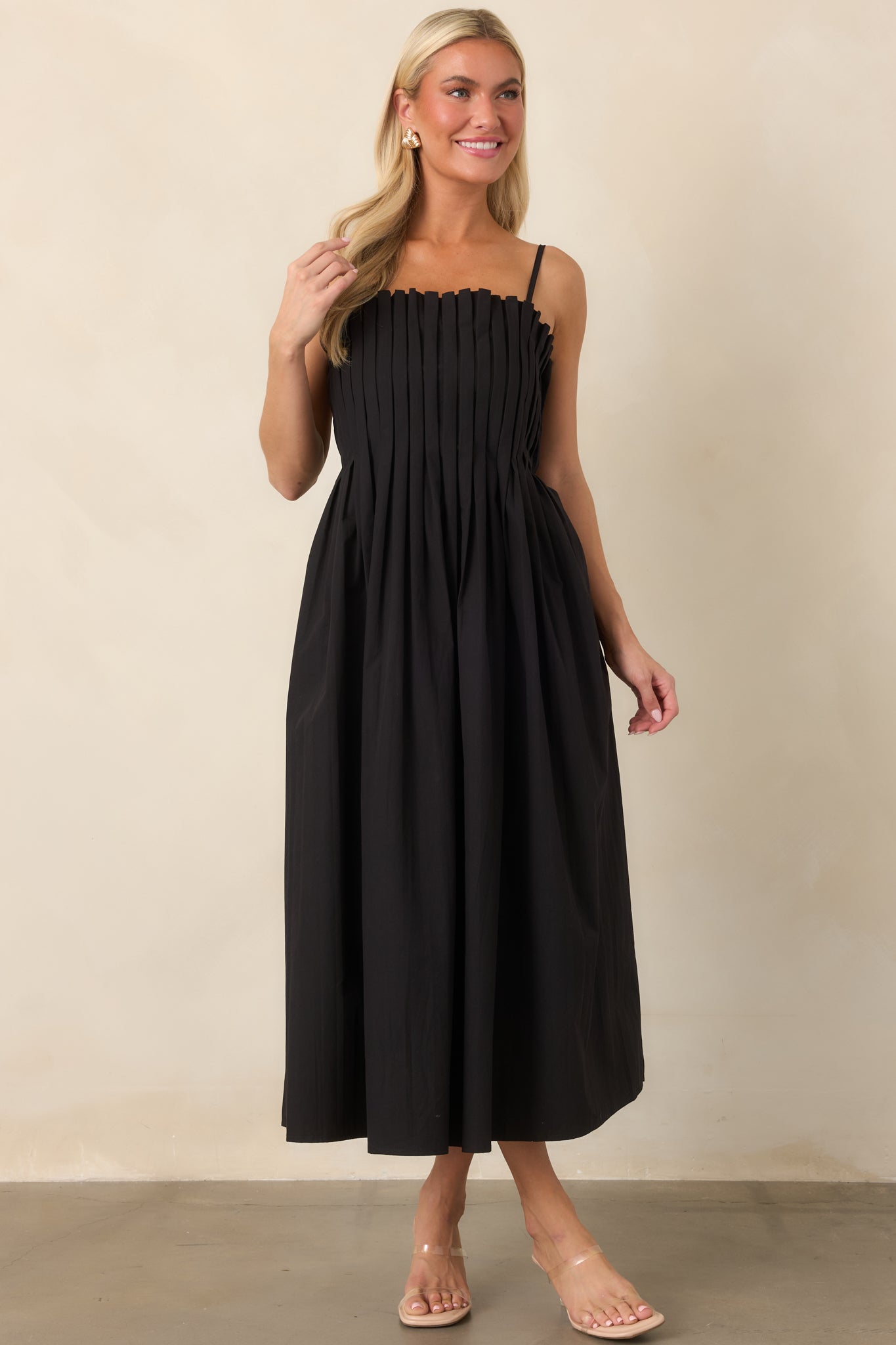 Black cotton midi dress highlighting the defined waist, finely pleated bodice, adjustable straps, and generously gathered skirt.