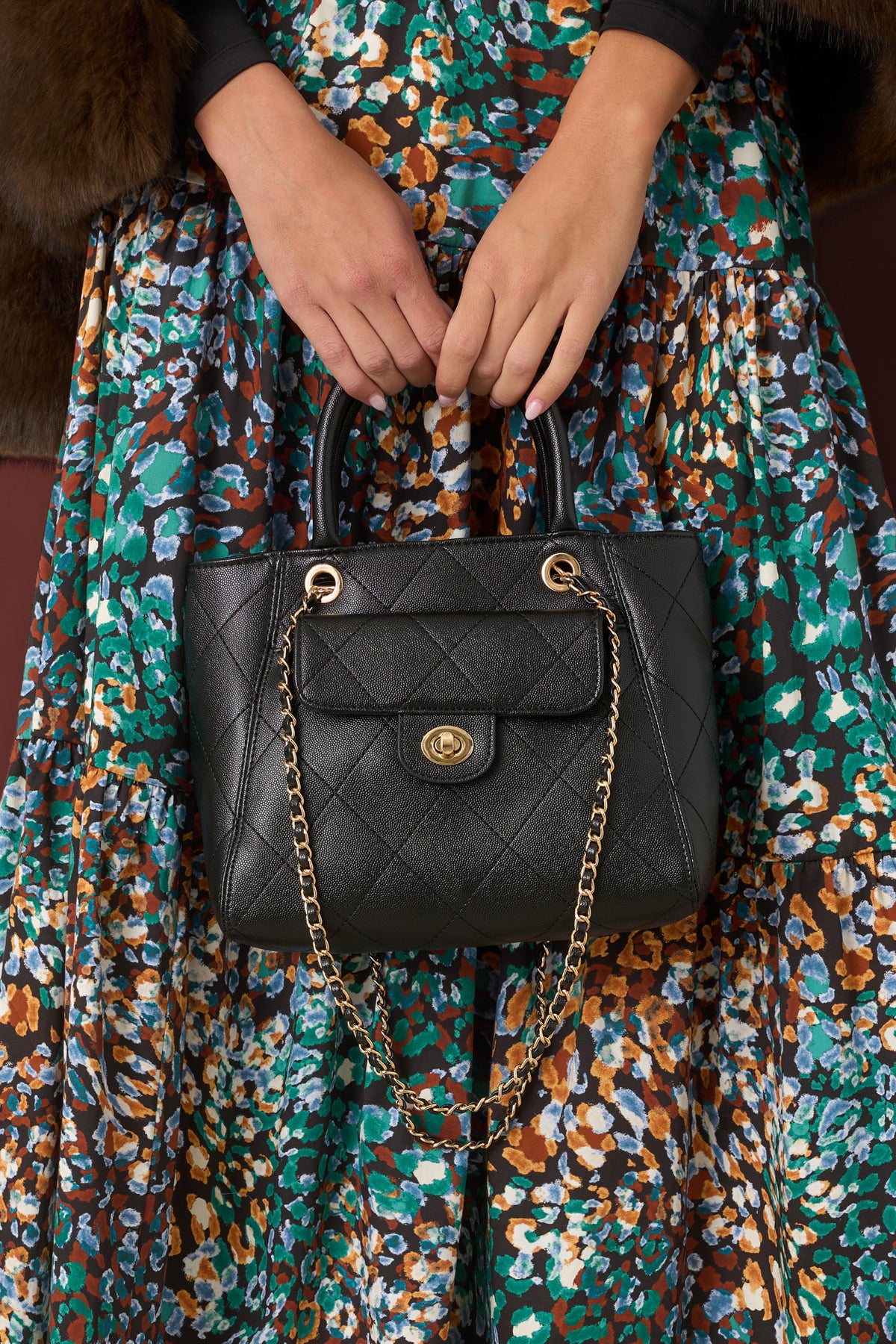 Close-up of a black diamond-quilted purse with textured detailing, a front flap pocket, gold-tone clasp, and chain strap.