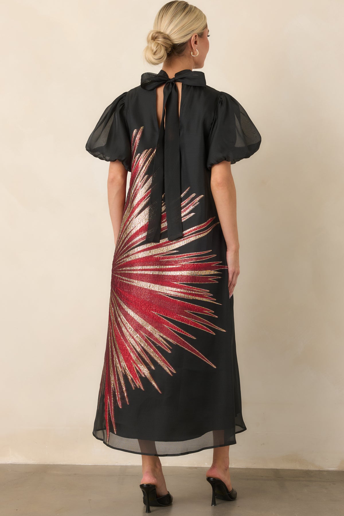 Black dress rear detail showing the back keyhole, elongated ties, sheer puff sleeves, and flowing A-line silhouette.
