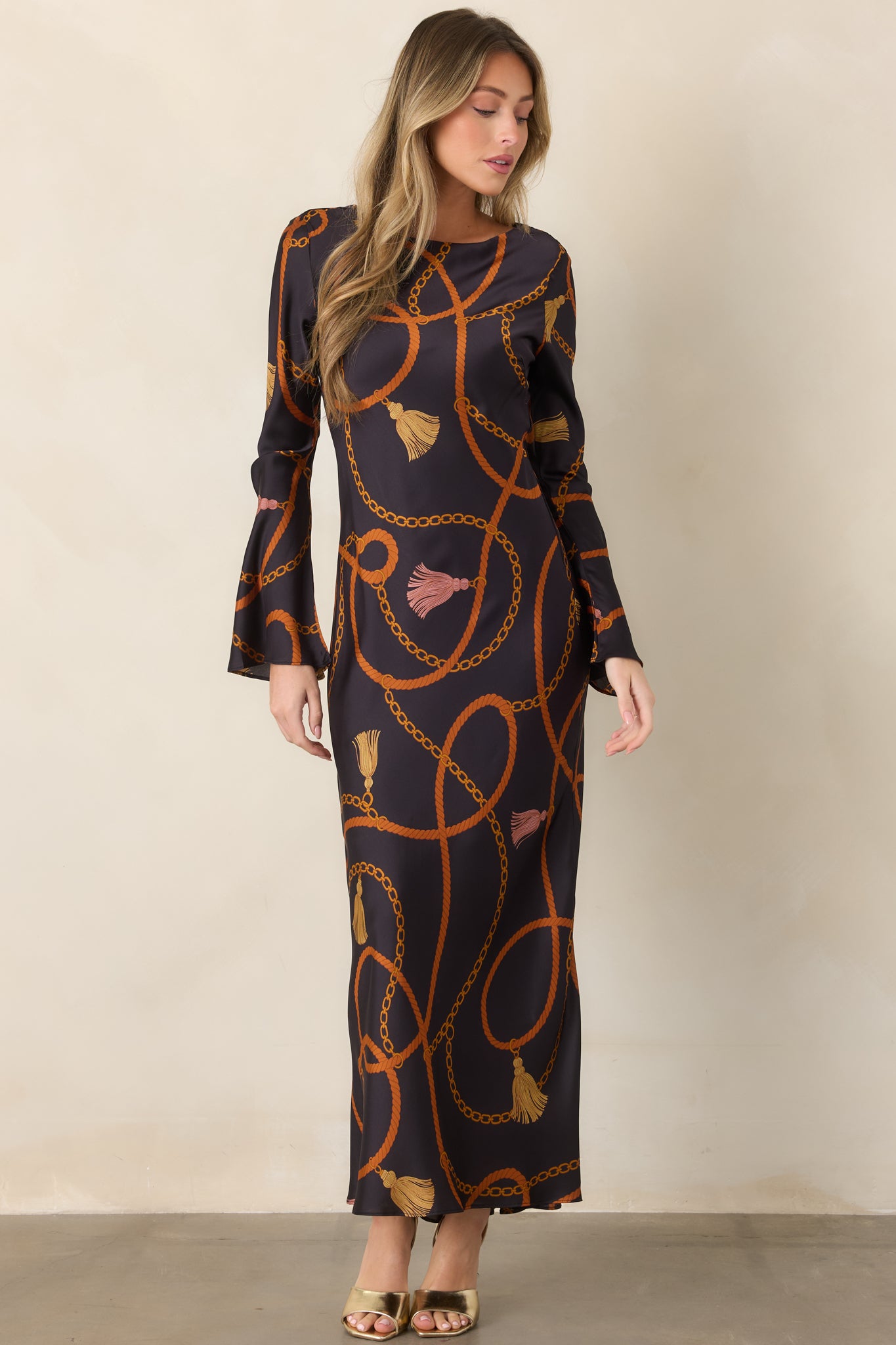 Equestrian-inspired black maxi dress showcasing its ornate rope, chain, and tassel pattern with a softly draped silhouette.