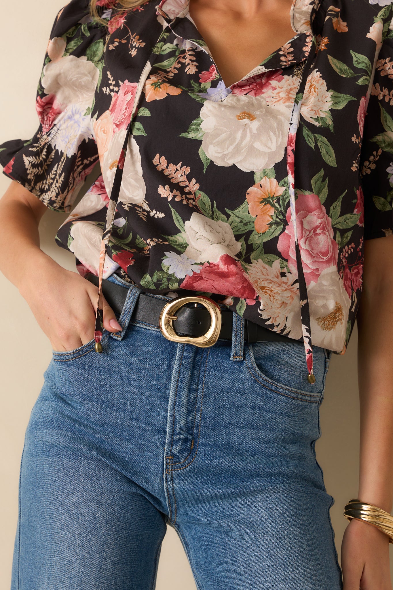 A cropped view of the black faux leather belt highlighting the hollow organic-shaped gold buckle.