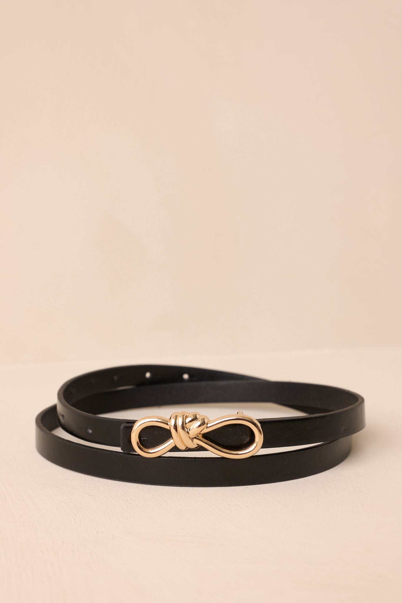 Black faux leather belt with slim design and gold rope-inspired interlocking buckle.