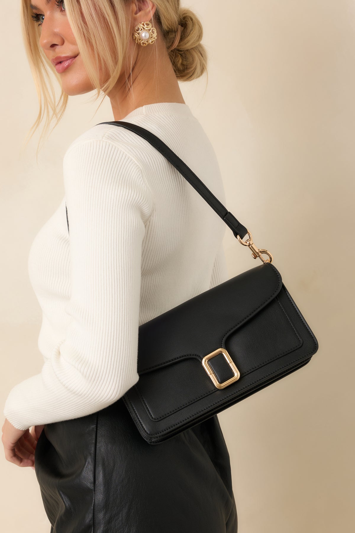 Black faux leather handbag with a structured rectangular shape, contoured envelope flap, and polished gold-tone buckle clasp.