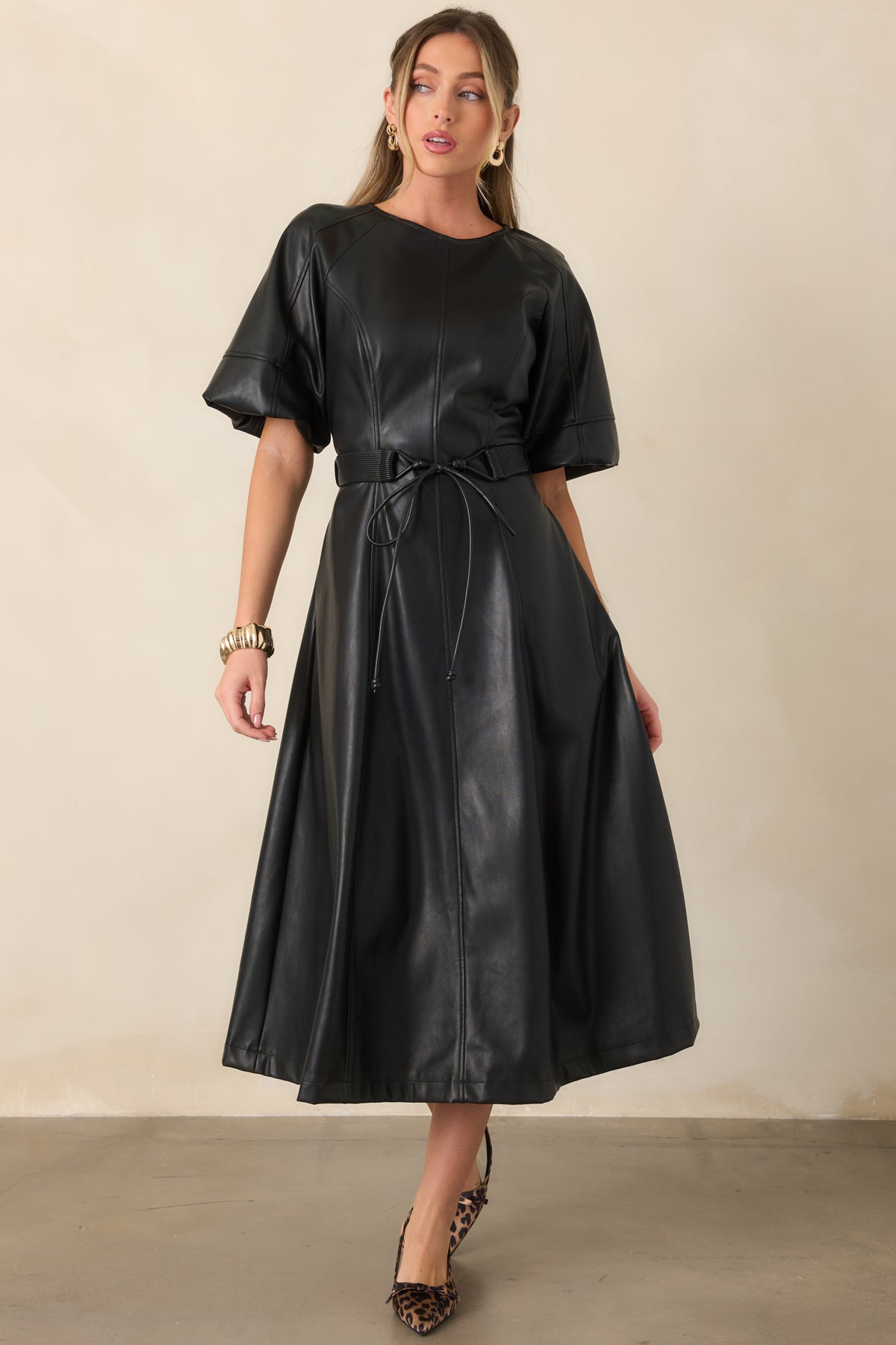 Black faux leather midi dress featuring clean vertical seams, a defined waist, and softly flared skirt.