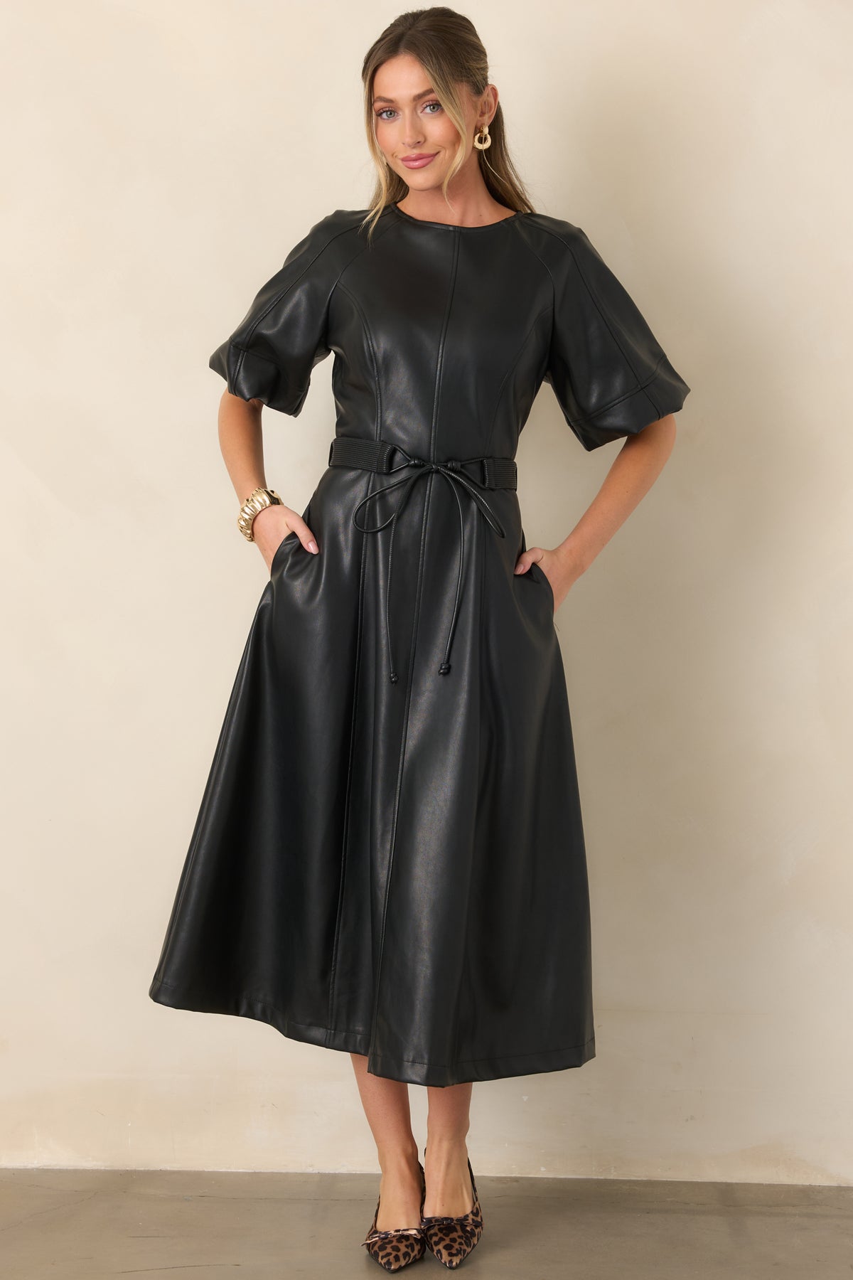 Black faux leather midi dress showcasing the short raglan sleeves, adjustable waist tie, and flowing A-line skirt.