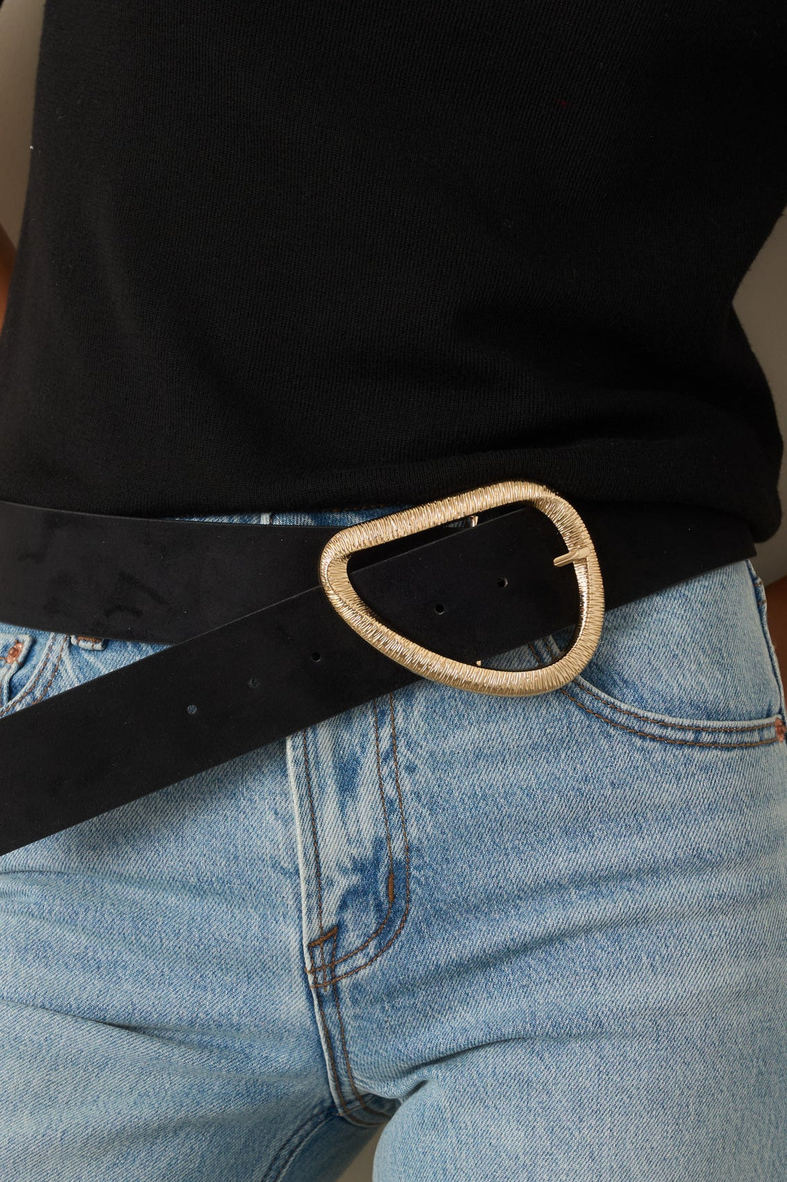 Close-up of a wide black faux suede belt featuring a textured gold-tone curved D-shaped buckle and adjustable holes.