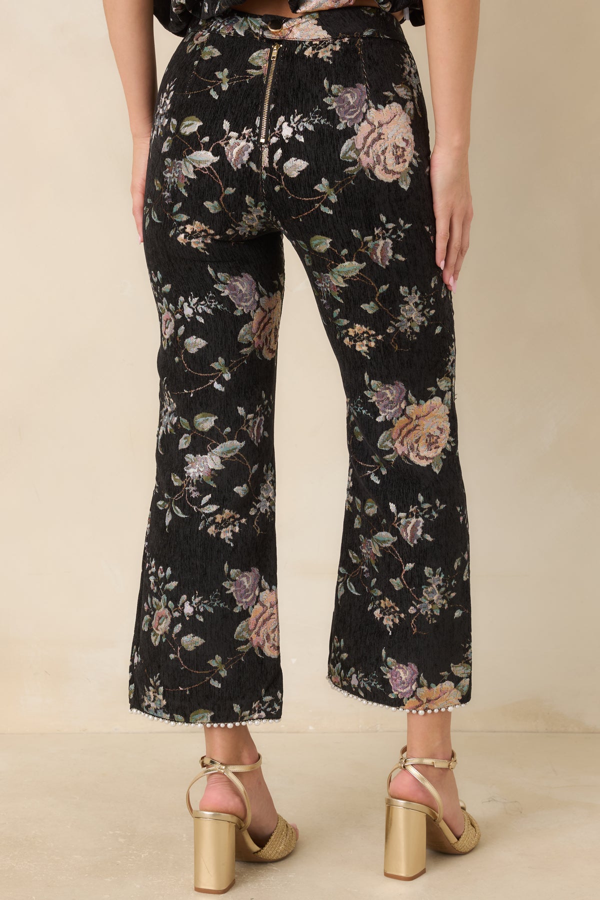 Rear of the black floral cropped pants showing the fitted silhouette, back zipper, and snap closure at the waistband.