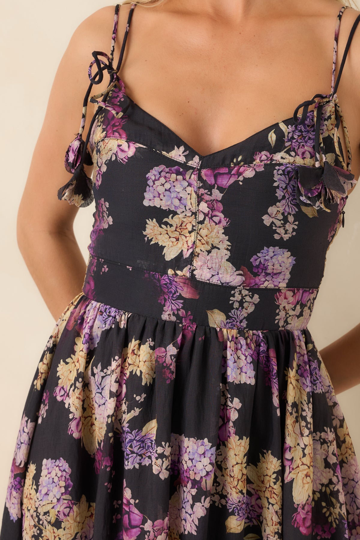 Close-up of the black floral dress’s dipped neckline and adjustable tie straps with decorative floral accents.
