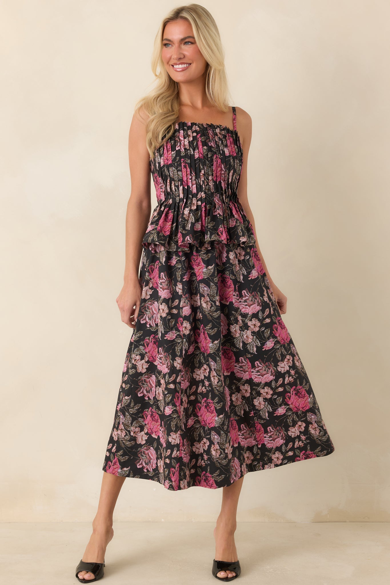 Black floral midi dress featuring a smocked back, layered peplum waist, and a softly flowing full skirt.