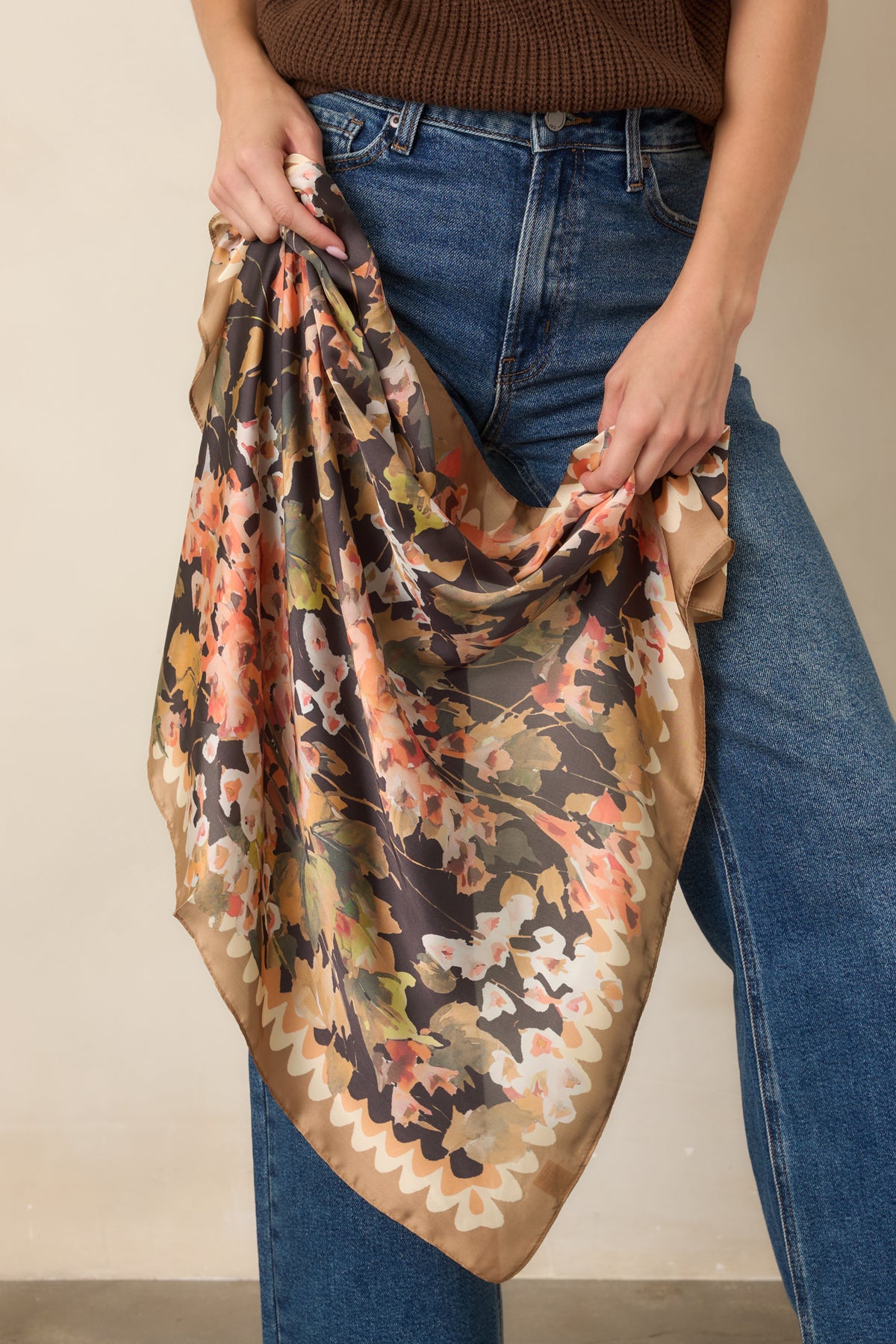 Black square scarf showcasing soft floral blooms in peach, coral, ivory, olive, and camel tones with a polished camel border.