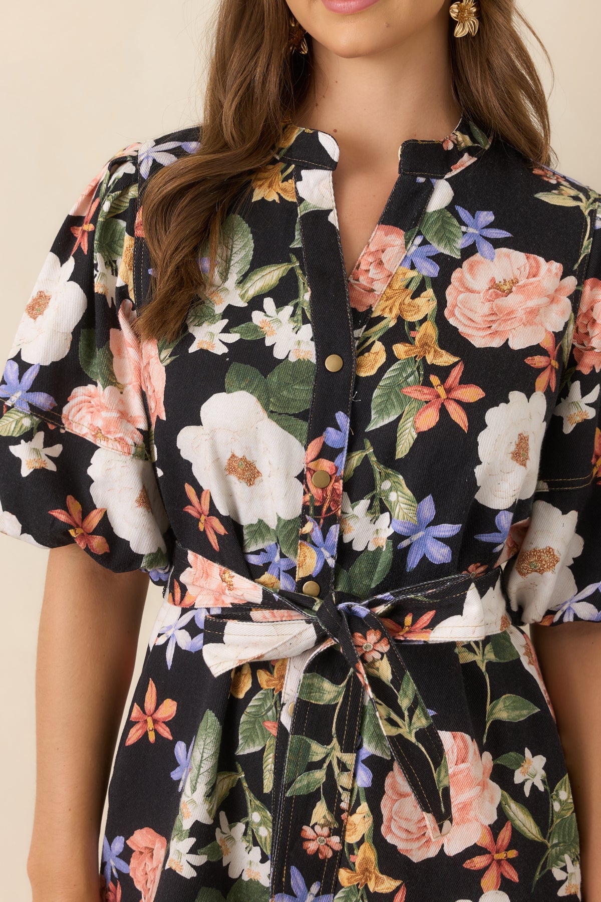 Black floral mini dress detail featuring the split neckline, gold-tone buttons, and colorful coral, lavender, and golden yellow blooms.