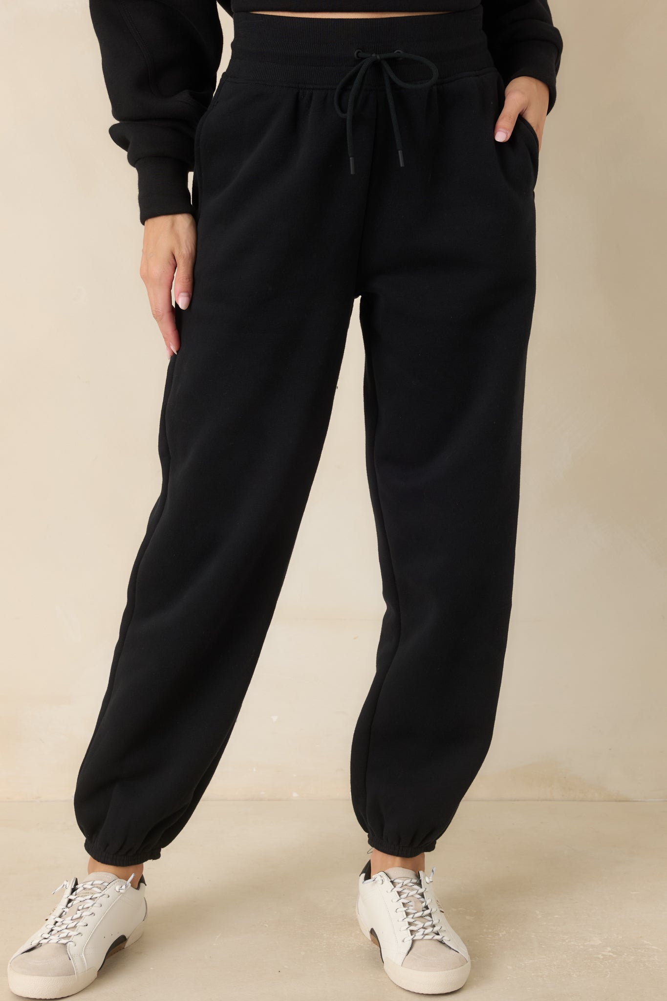 Close view of the black joggers highlighting the ribbed waistband, adjustable drawstring, and smooth cotton-blend fleece fabric.