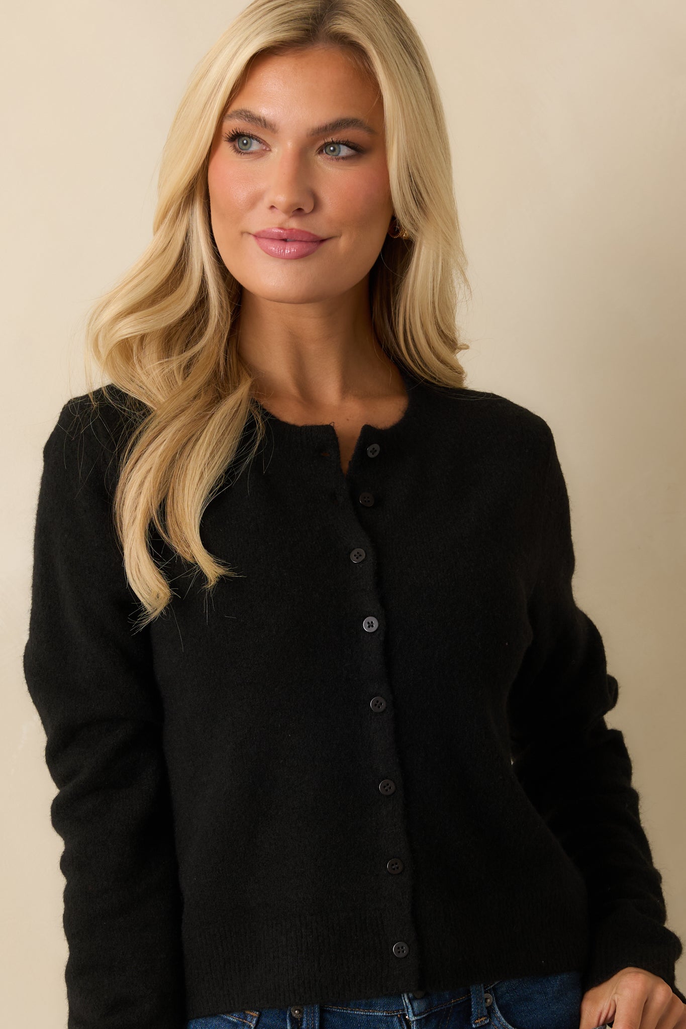 Close look at the round neckline and front buttons set against the smooth black knit.