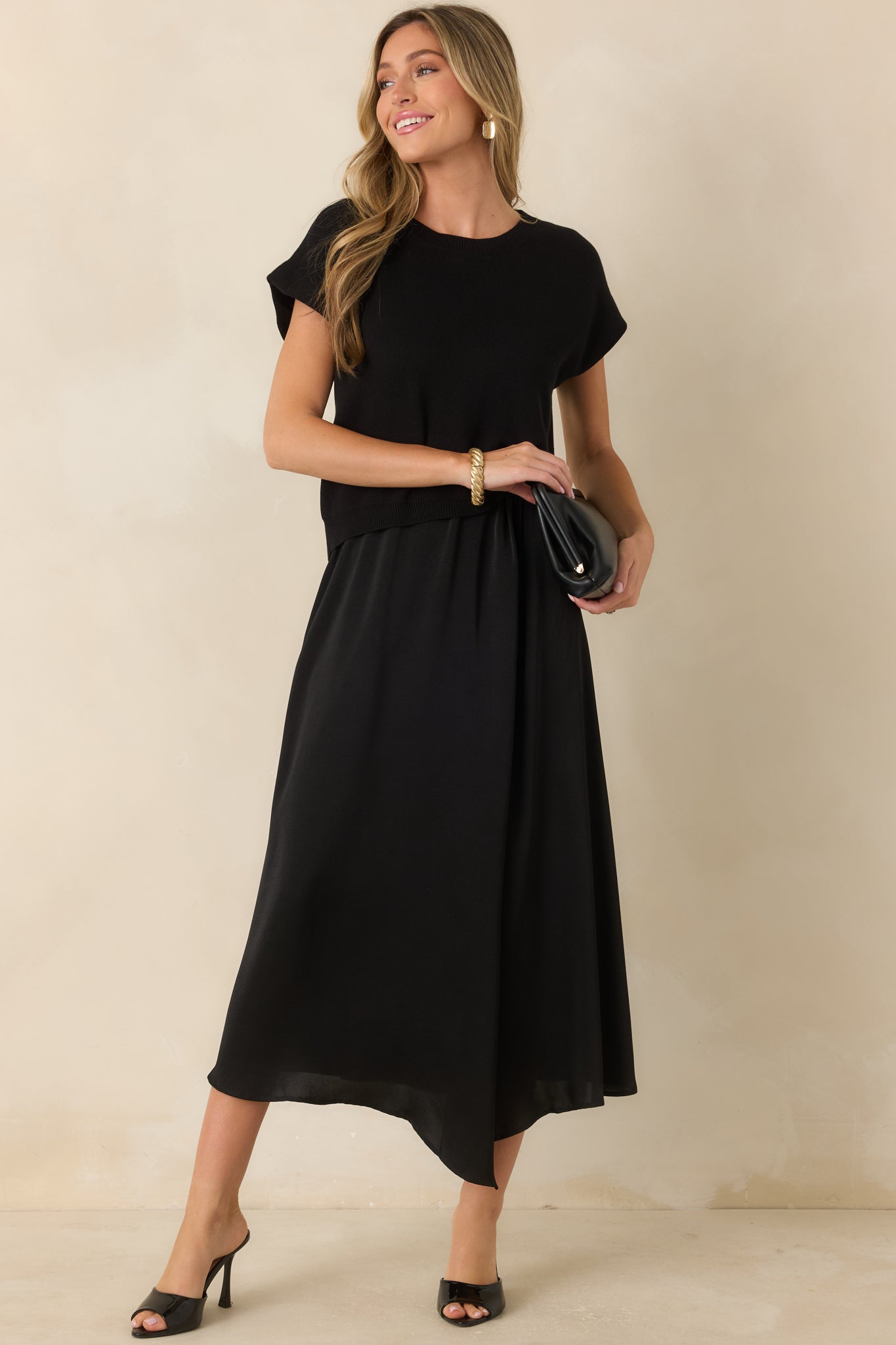 Black knit sweater with cap sleeves, a ribbed neckline, and a relaxed fit finished with a subtle cinched front hem.