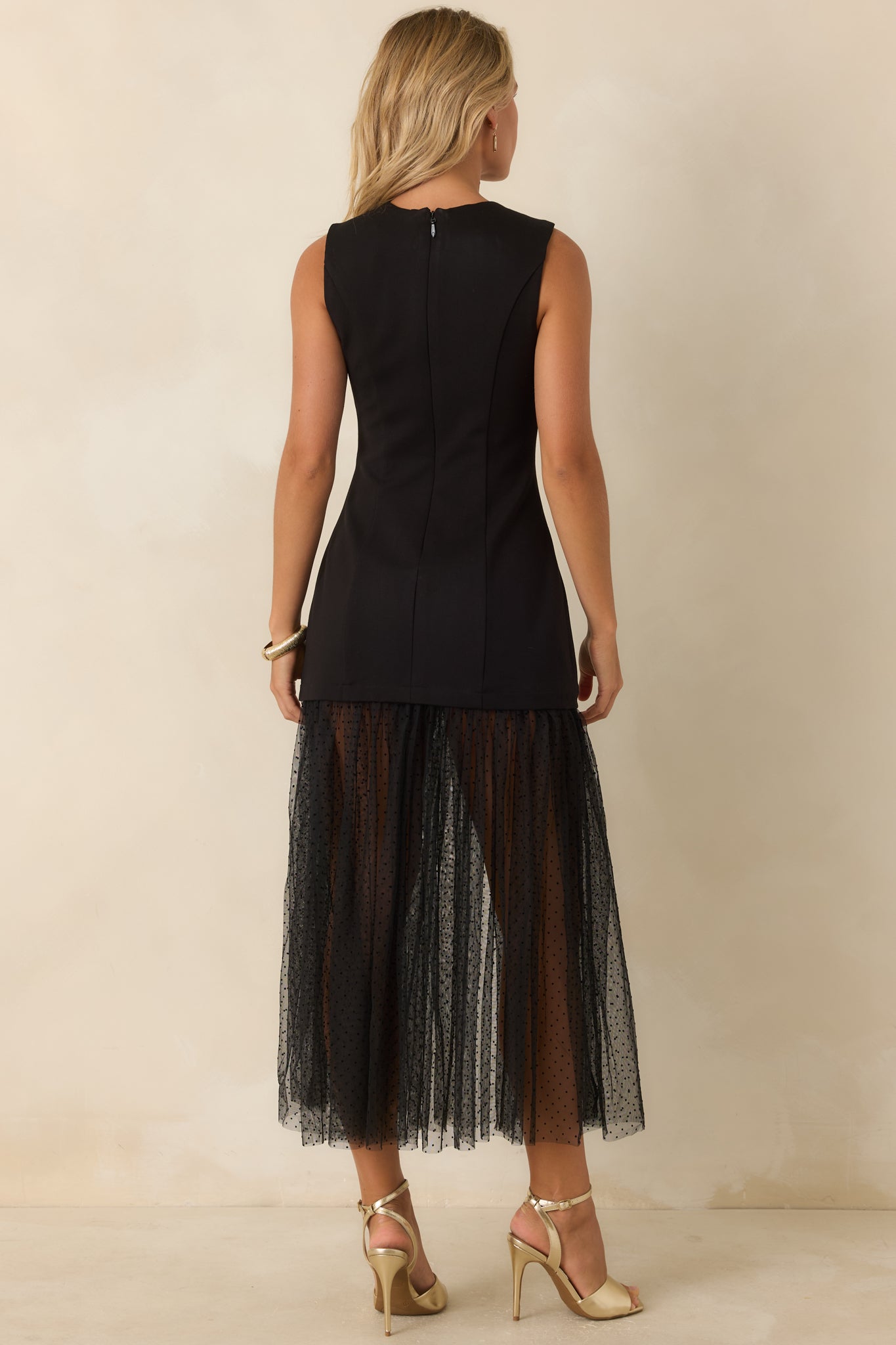 Rear view of the black midi dress showcasing the sleeveless silhouette, concealed back zipper, tailored shaping, and sheer Swiss dot mesh hem.
