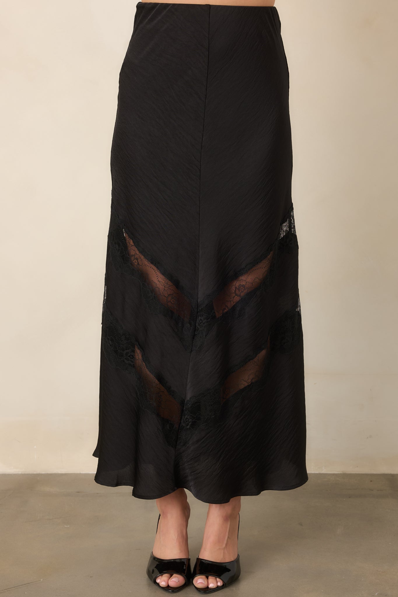 Black midi skirt displaying tonal lace insets arranged in angled chevron patterns through the lower skirt.