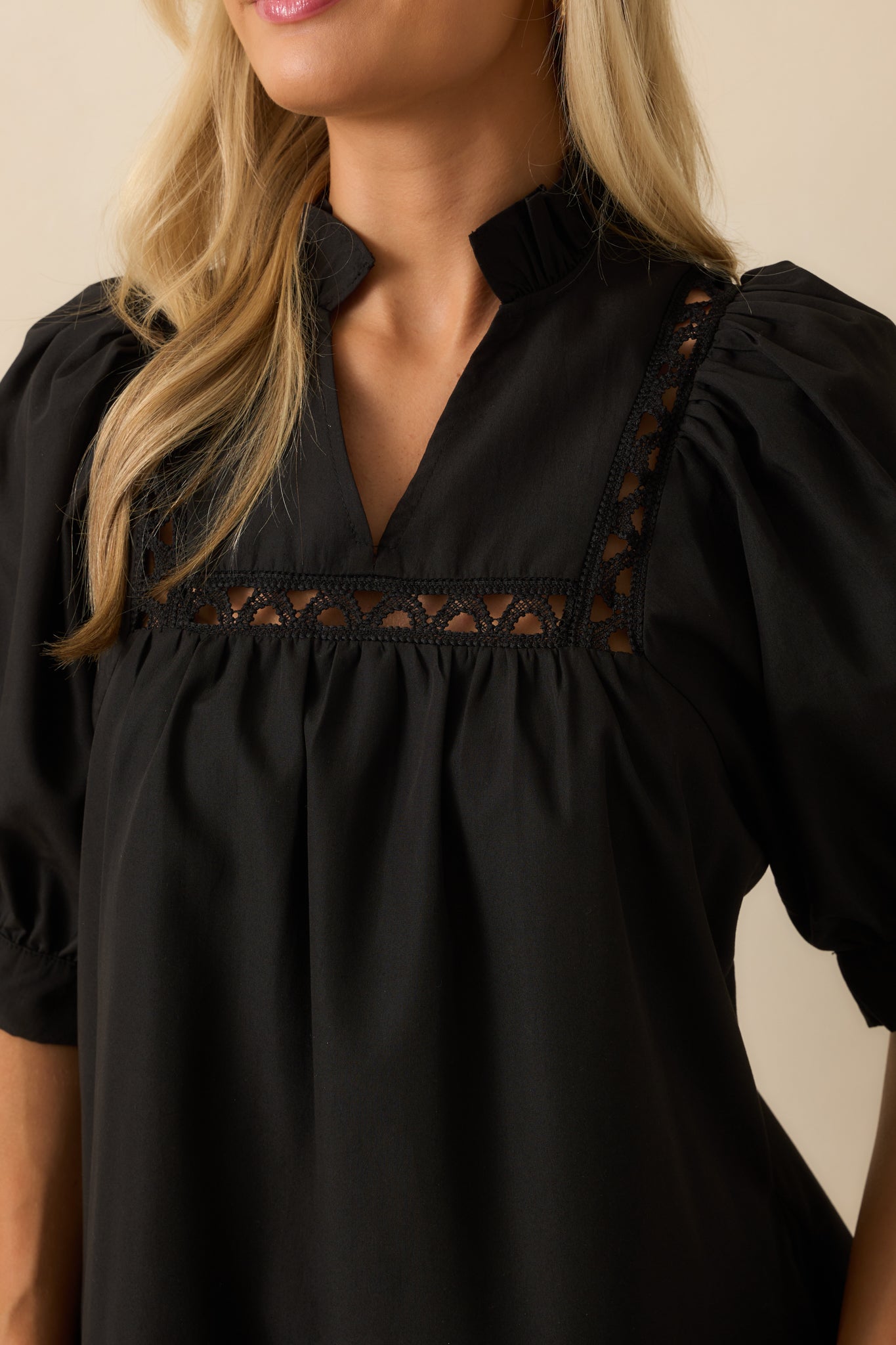Focused view of the ladder lace inserts and ruffle-trimmed split v-neckline on black mini dress, showing puff sleeves and tiered hem texture.