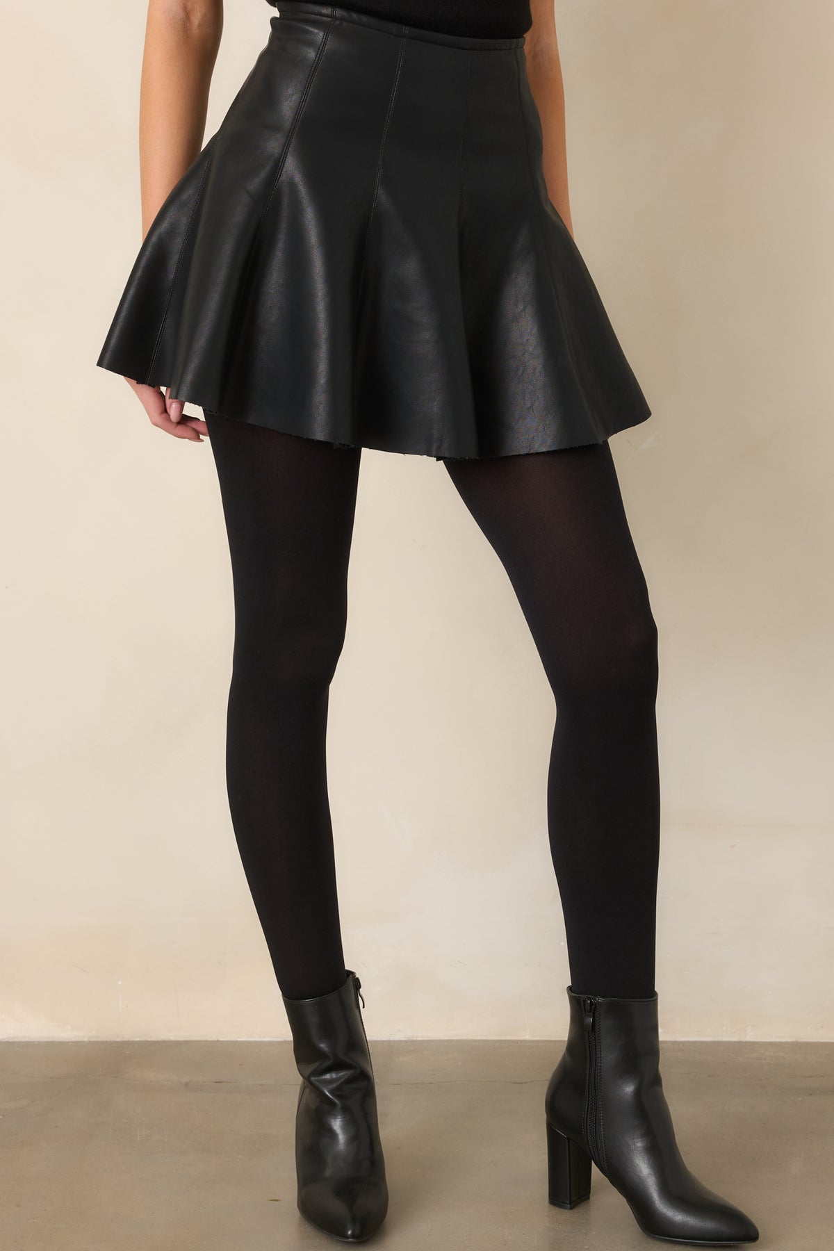 Black mini skirt detail showing its sleek faux leather finish and flared construction.