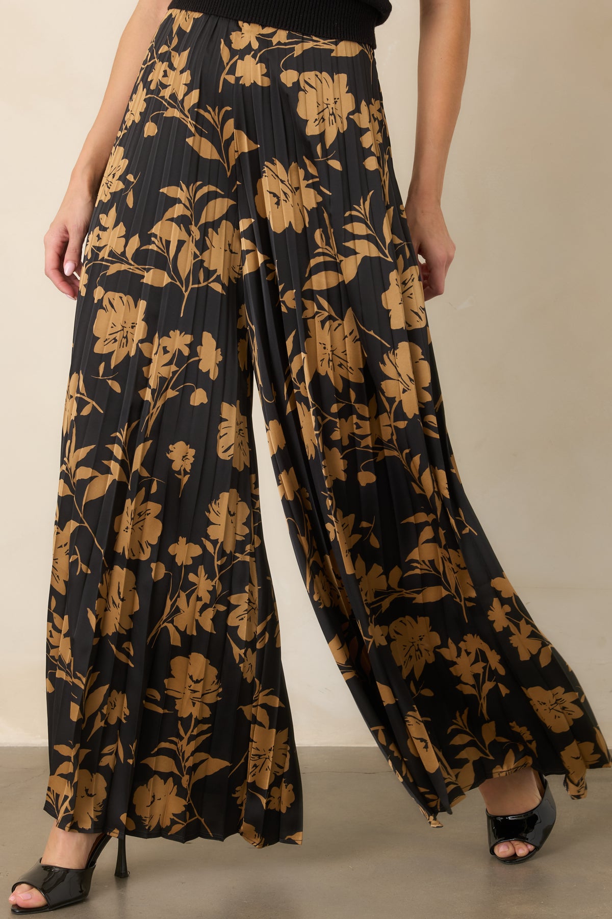 Black pants highlighting golden floral silhouettes and finely textured accordion pleats across the wide legs.
