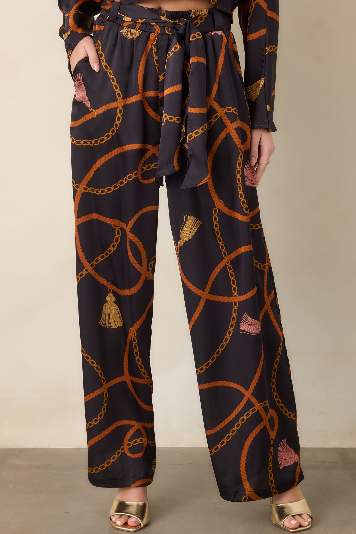 Close view of the black pants highlighting the coordinating scarf-tie belt and intricate rust and gold print.