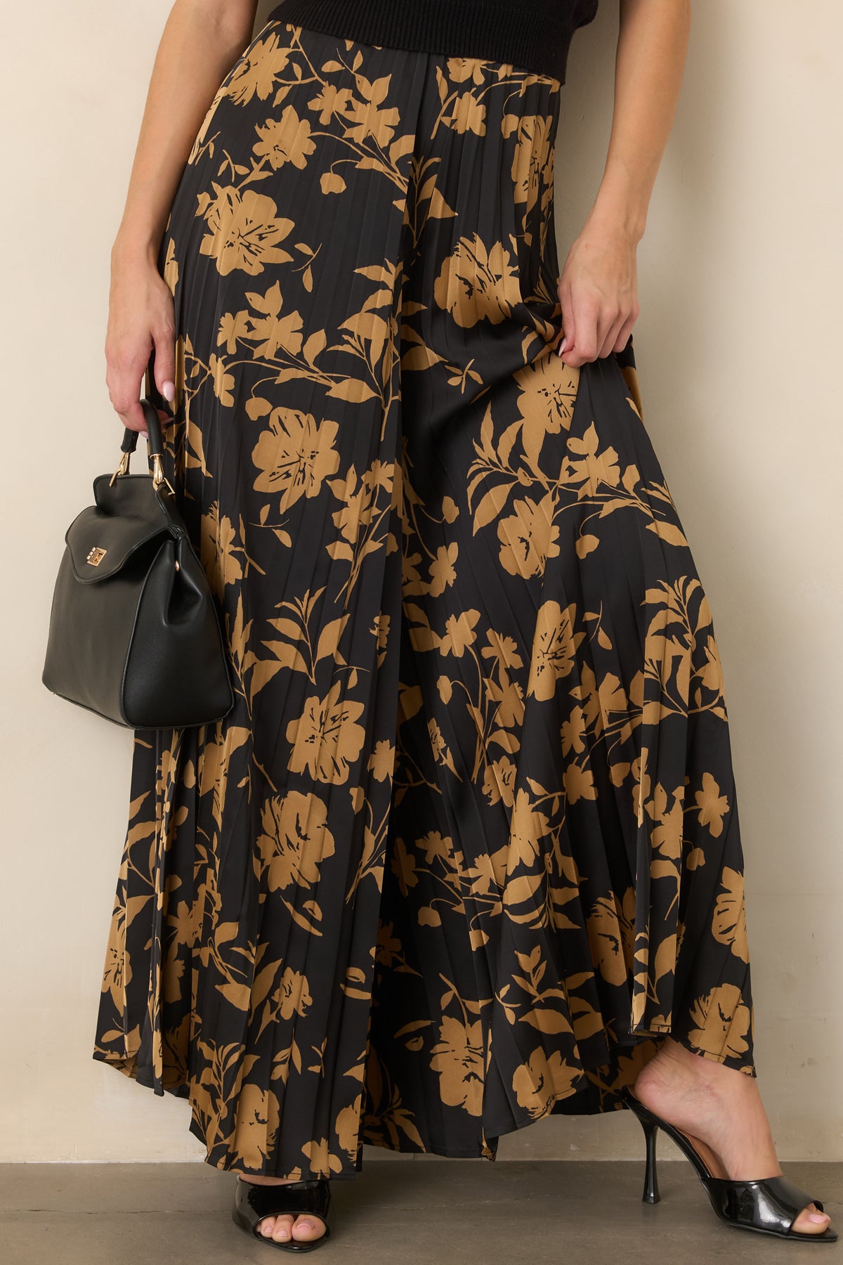 Black pleated pants showcasing the flowing wide-leg shape and scattered golden floral silhouettes.
