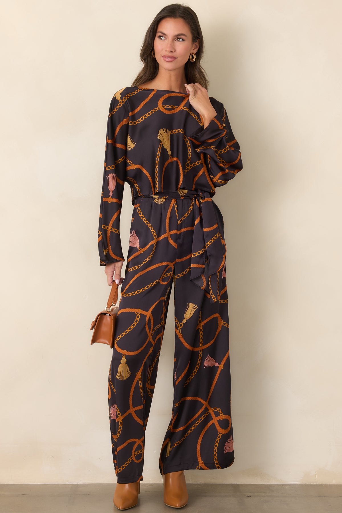 Black satin-feel pants featuring an allover rust, gold, and blush rope, chain, and tassel print with a relaxed wide-leg silhouette.
