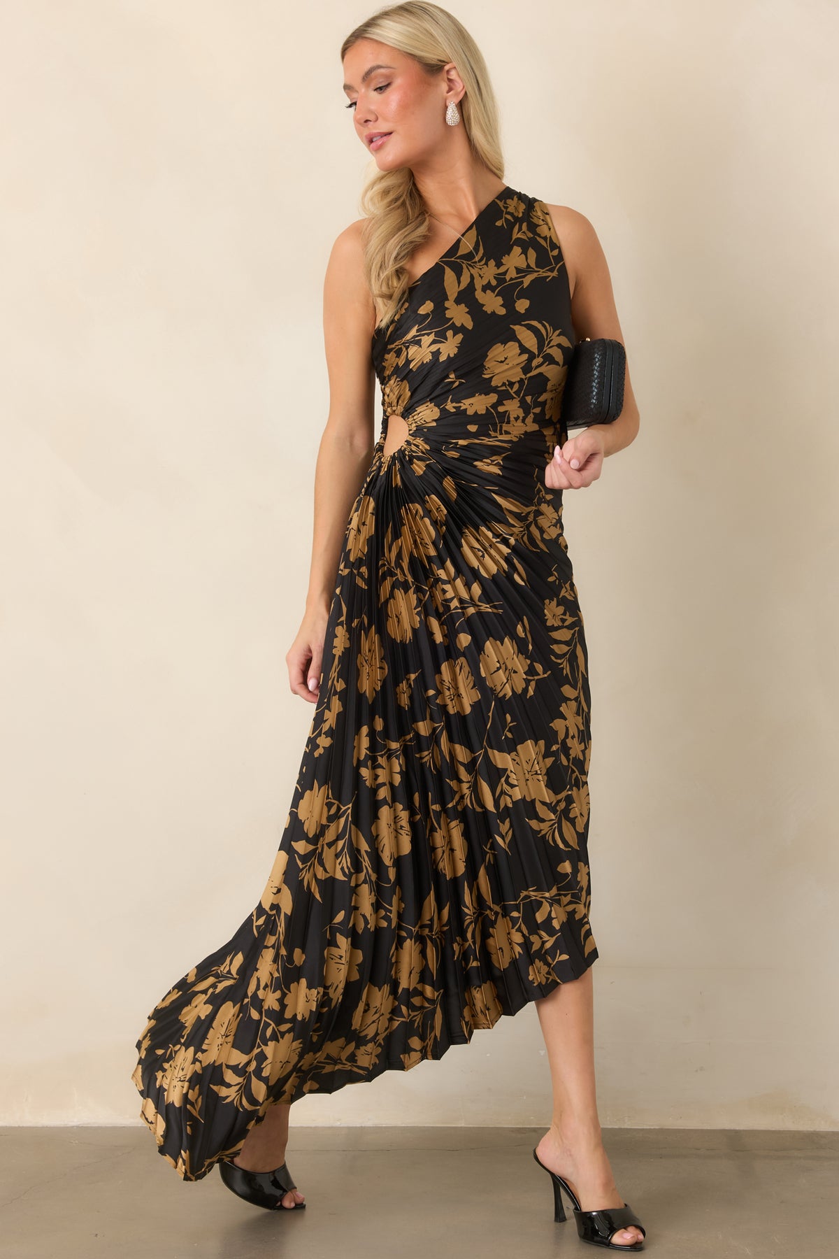 The one-shoulder dress combines lustrous black satin with golden floral motifs, waist ruching, and a flowing uneven hem.