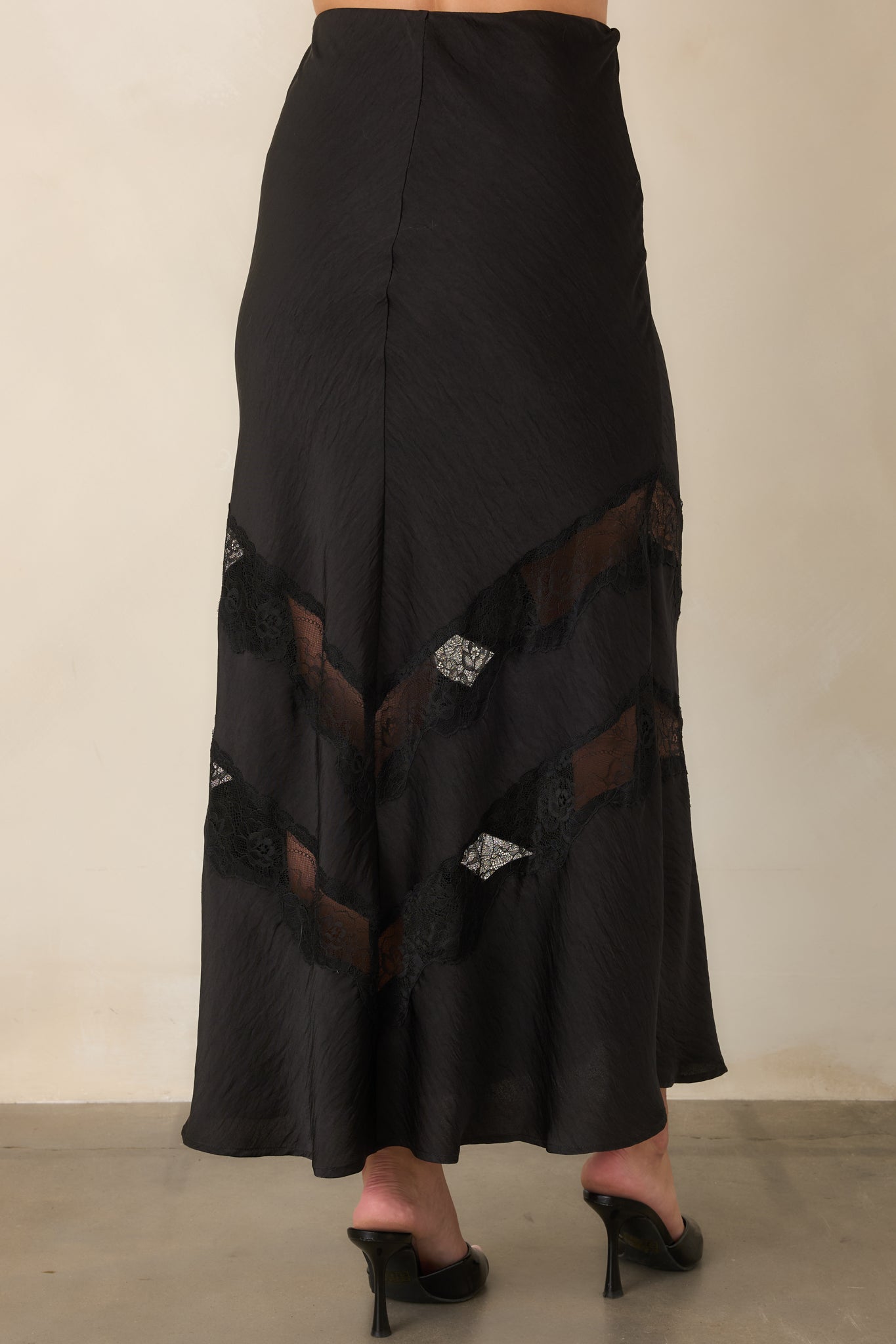 Rear view of the black satin midi skirt highlighting its smooth fitted waist, fluid drape, and polished finish.