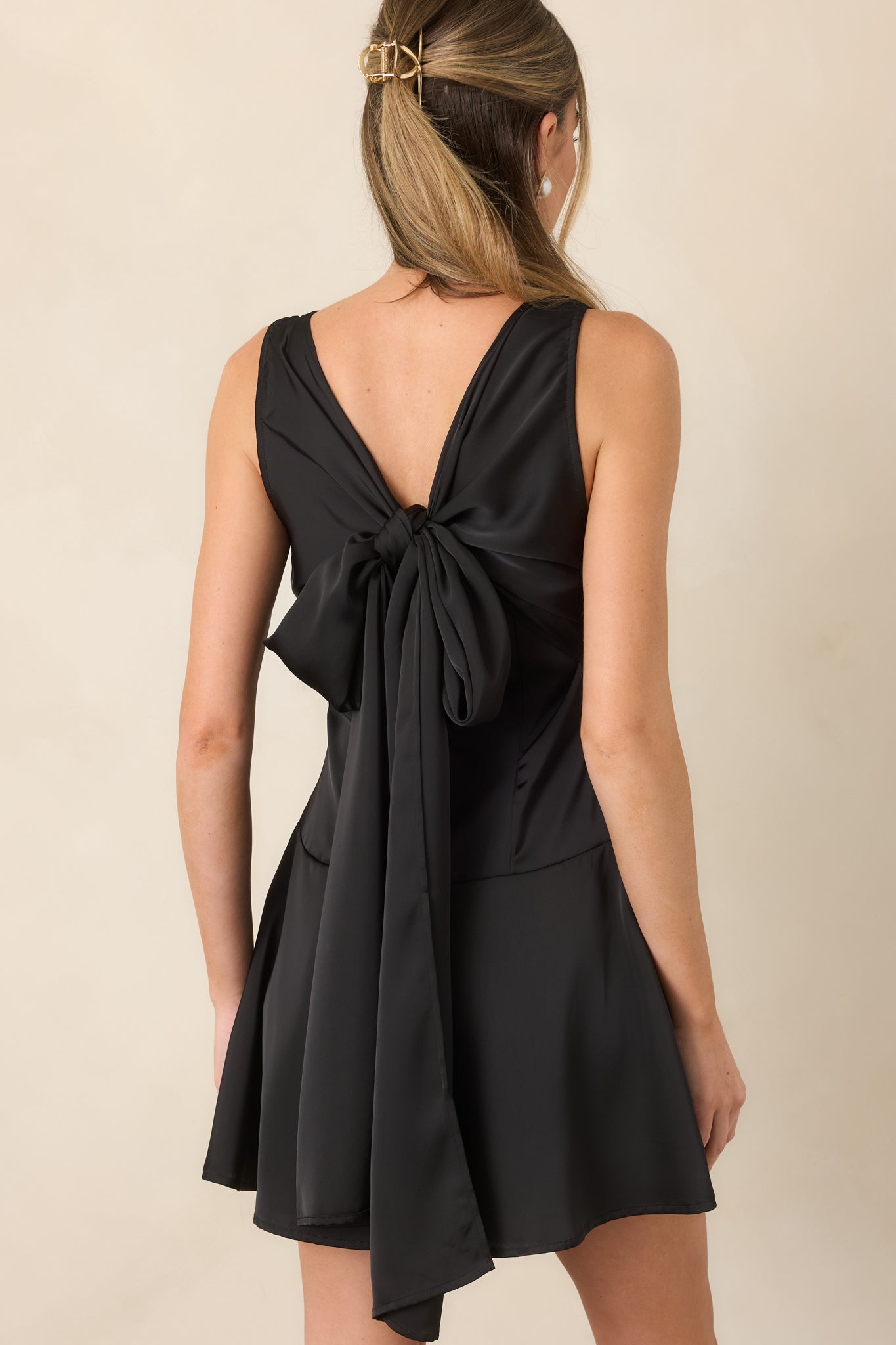 Rear view of the black satin mini dress featuring a deep V-back and oversized self-tie bow.