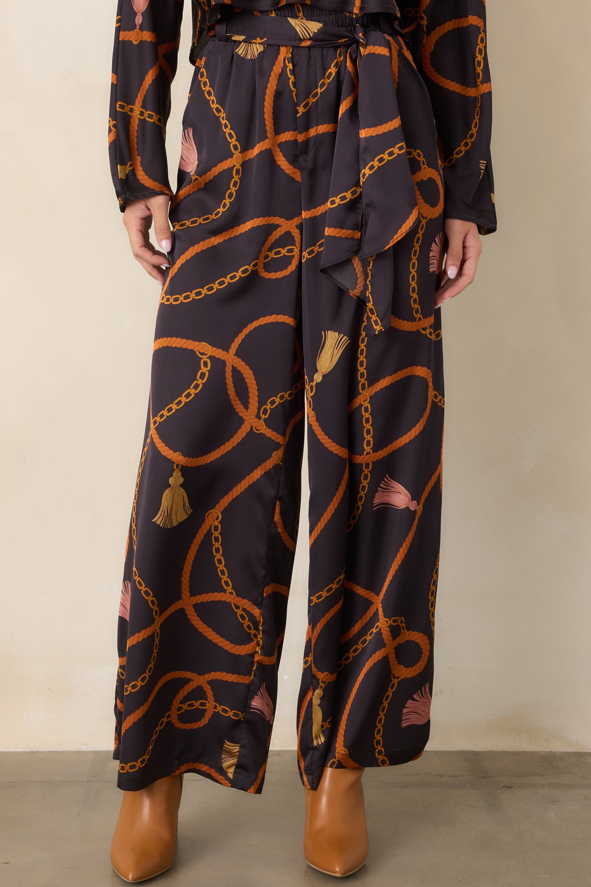 Satin-feel black pants featuring functional side pockets and an allover print of looping ropes, chains, and tassels.