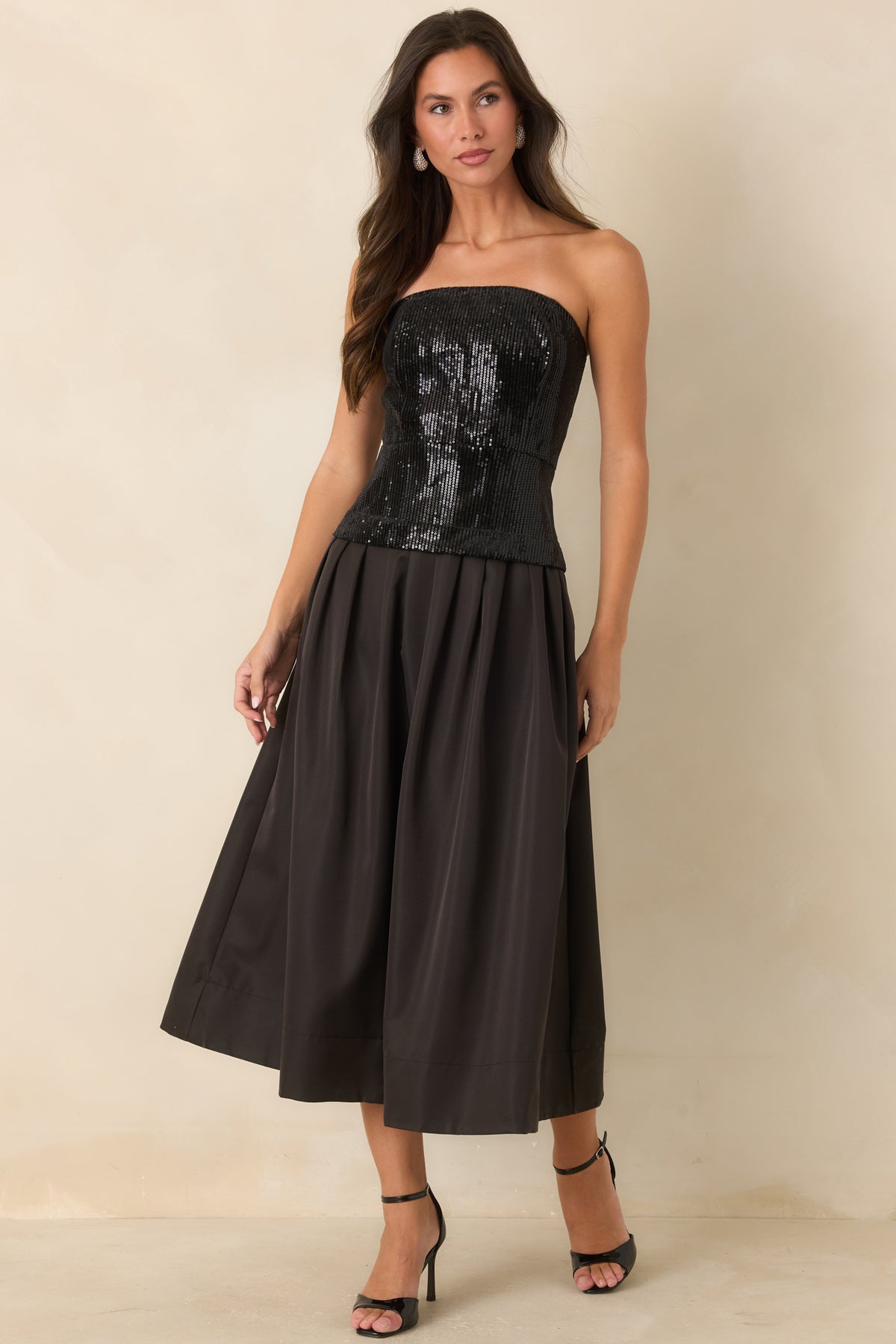 Black midi dress showcasing the contrast between its fitted sequin bodice and pleated skirt.