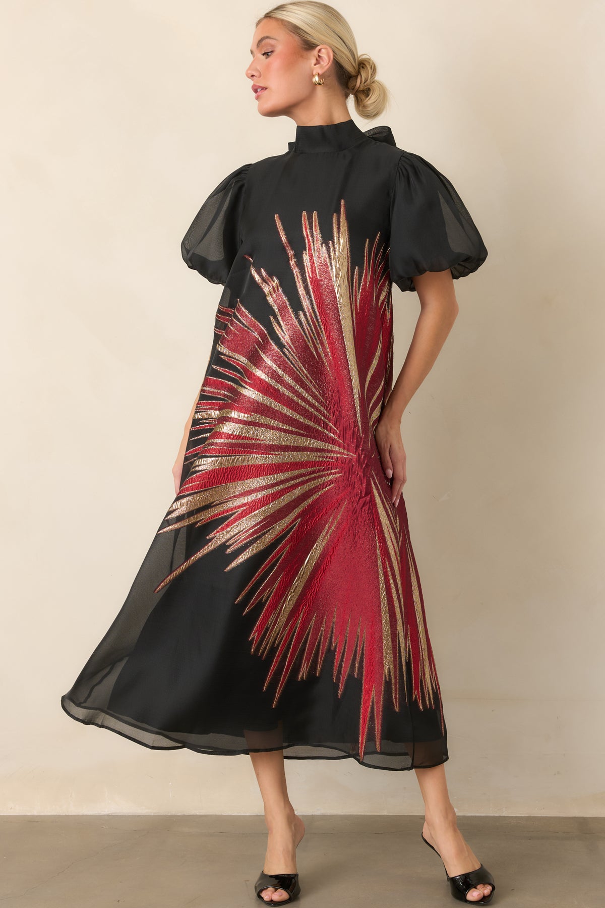 Sheer black midi dress featuring a shimmering red and gold metallic starburst design, sheer puff sleeves, and a flowing A-line silhouette.