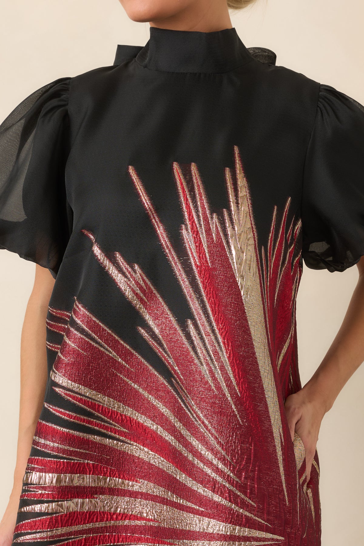 Close-up of the sheer black overlay with shimmering red and gold metallic starburst detailing and voluminous sleeve texture.