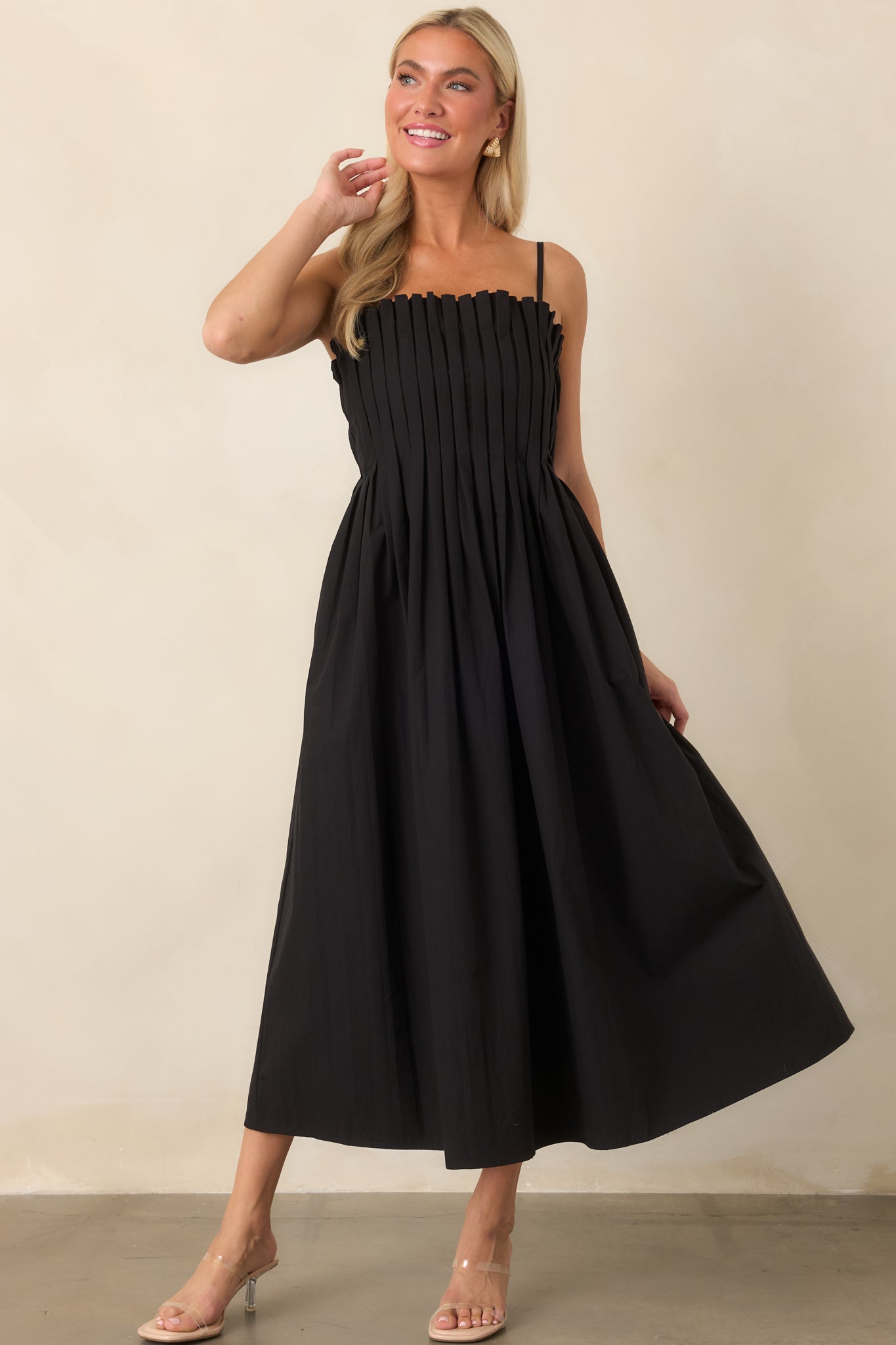 Full black midi silhouette with a clean square neckline, fitted upper bodice, and softly voluminous skirt with practical side pockets.