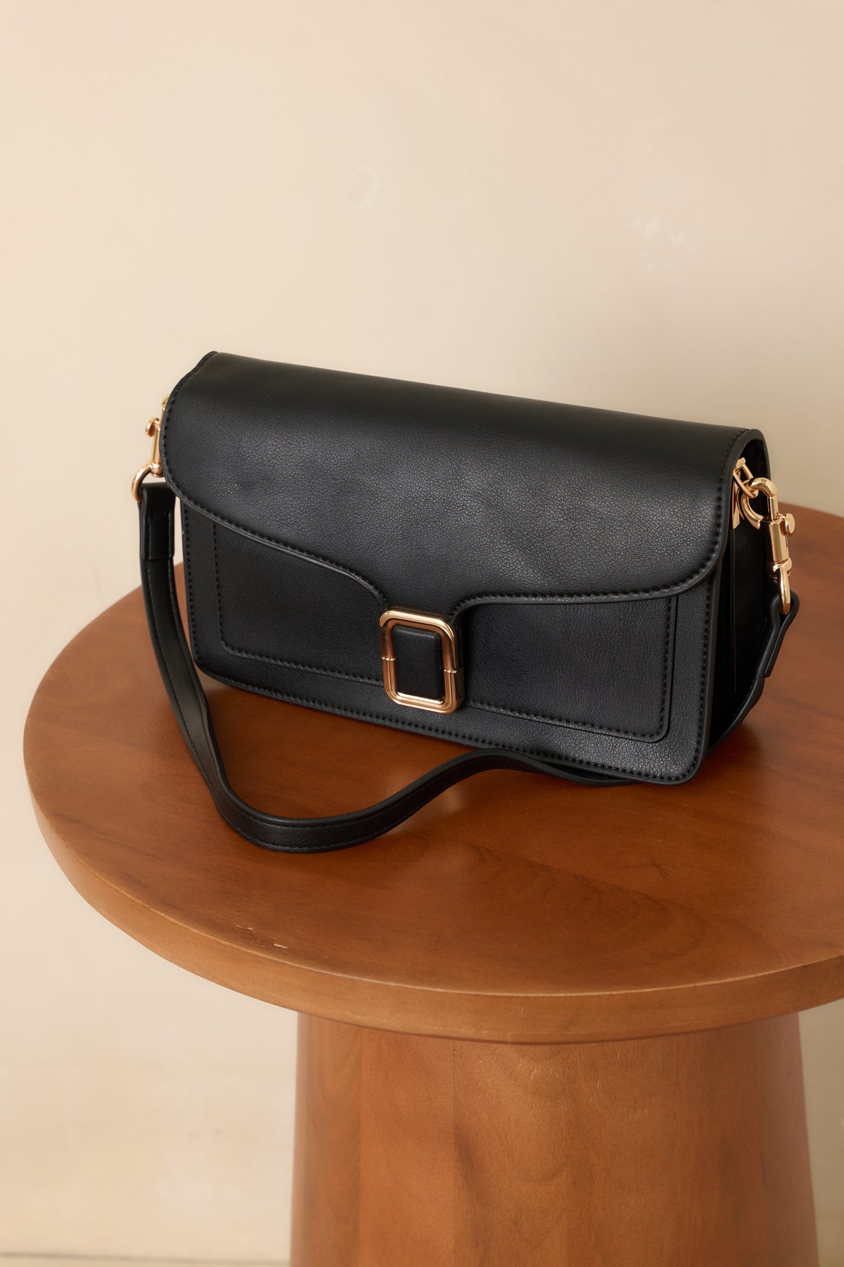 Structured black handbag featuring smooth faux leather, tonal edge stitching, and a detachable strap with gold-tone clips.