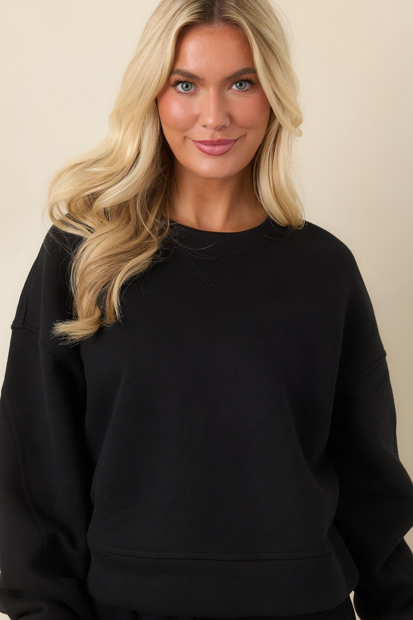 Close view of the black sweatshirt highlighting the ribbed crew neckline, stitched V-inset, and soft fleece texture.
