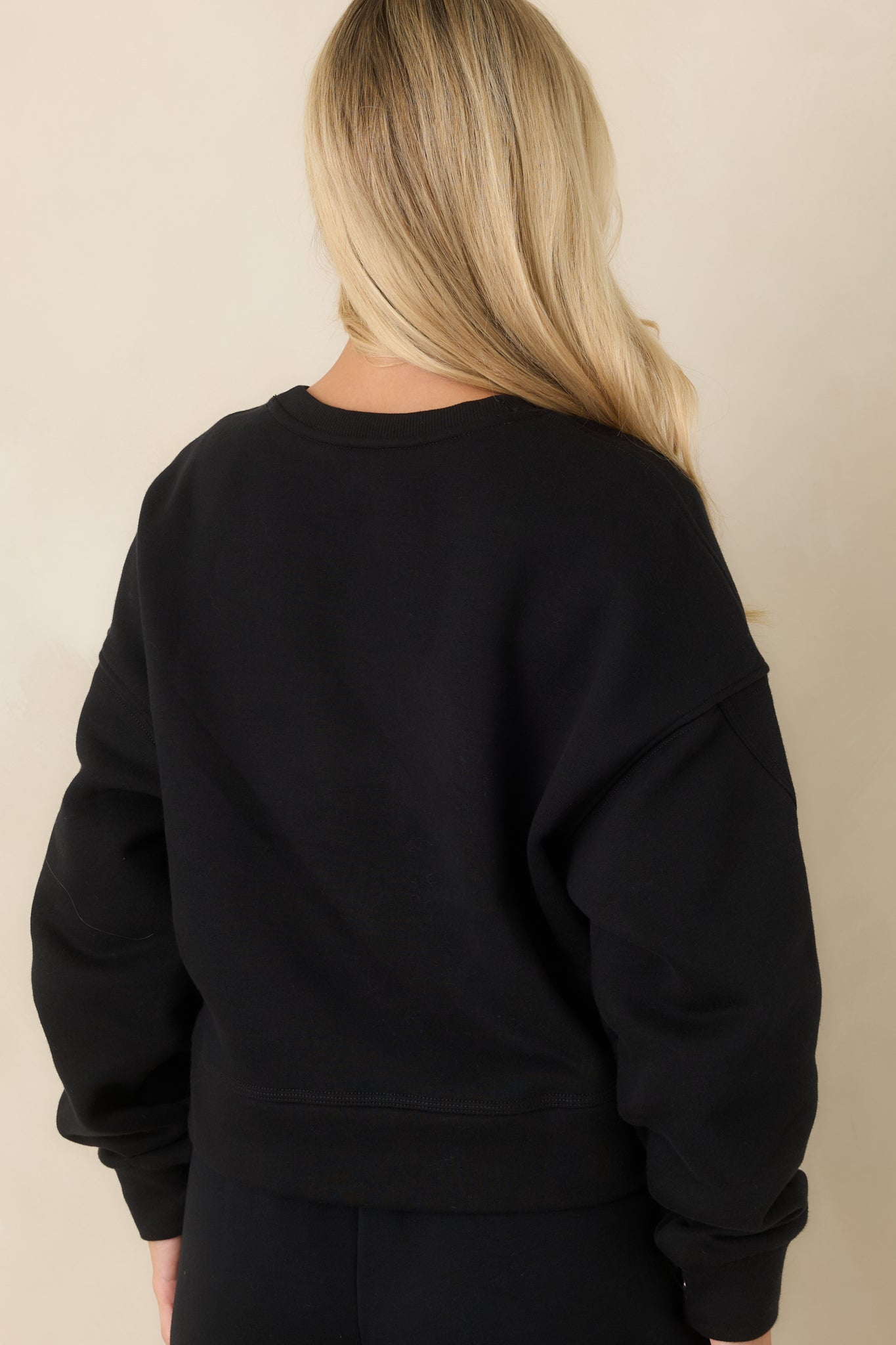 Rear view of the black fleece sweatshirt featuring dropped shoulders, long sleeves, a horizontal back seam, and a banded hem.
