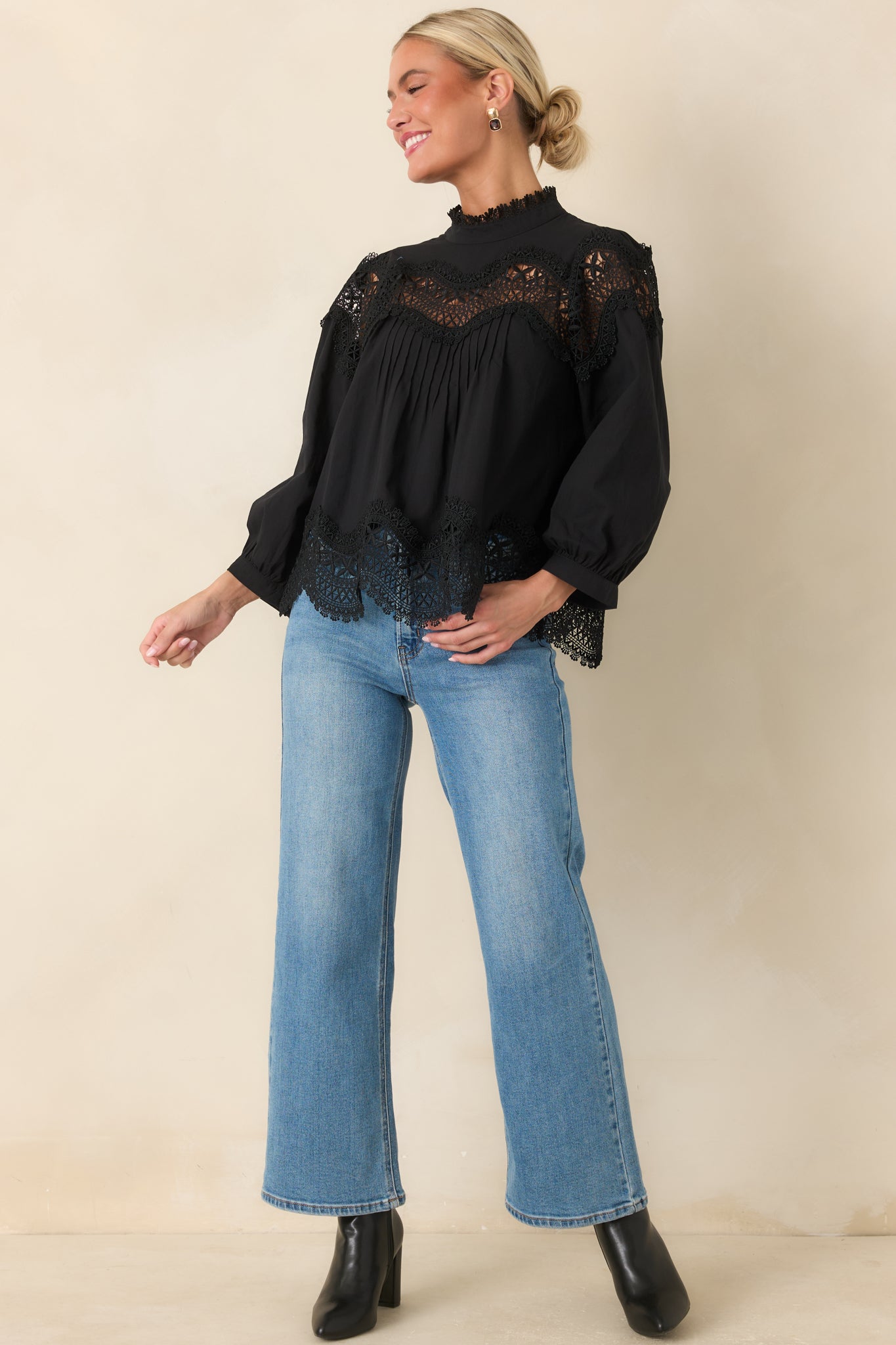Black top featuring a high neckline, balloon sleeves, lace detailing, and a polished relaxed shape.