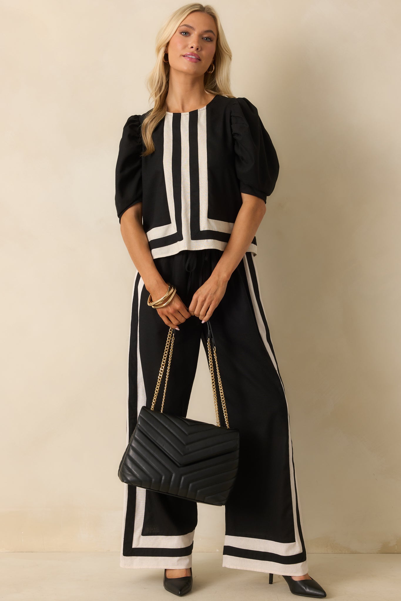 Wide-leg black pants with elastic waistband and adjustable tie, accented with ivory and black trim throughout, displayed front-facing.