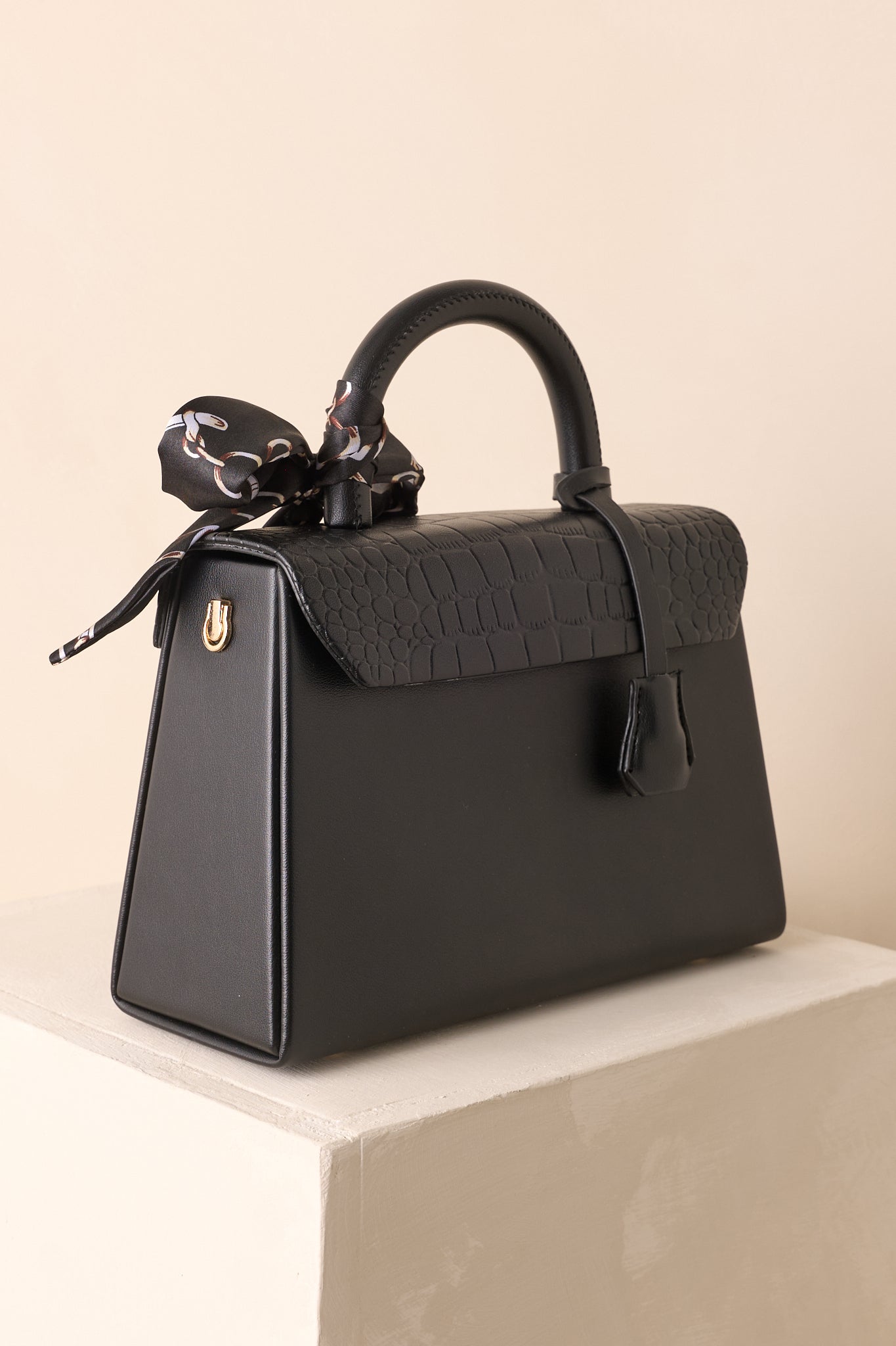 Back view of black handbag showing smooth faux leather surface and the smooth handle.