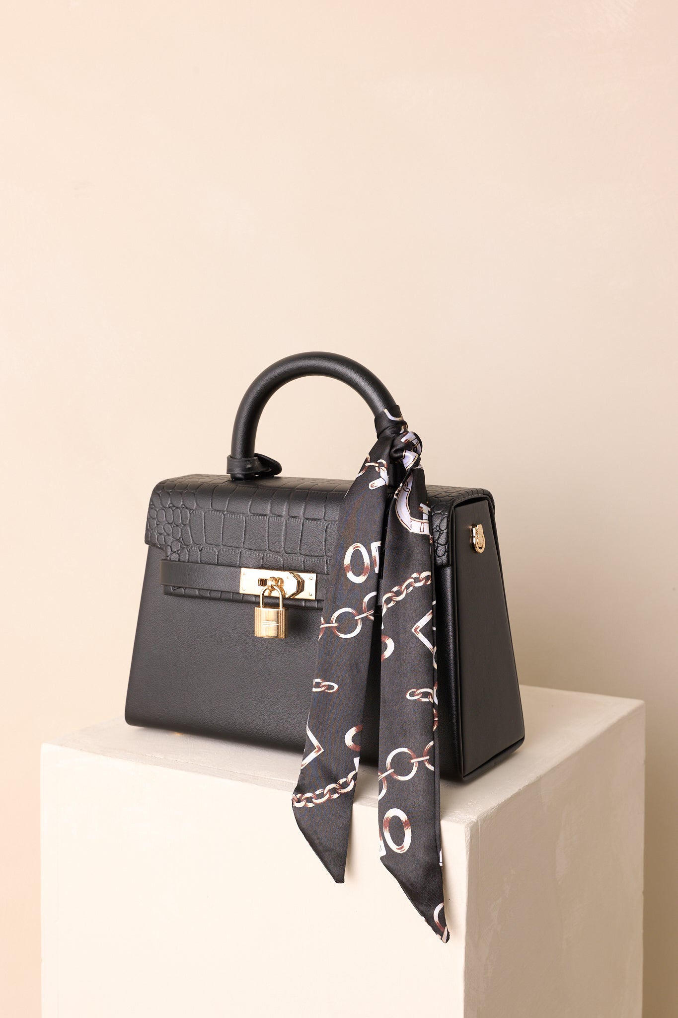 A full view of the black structured handbag with tan faux leather and a decorative self-tie scarf.