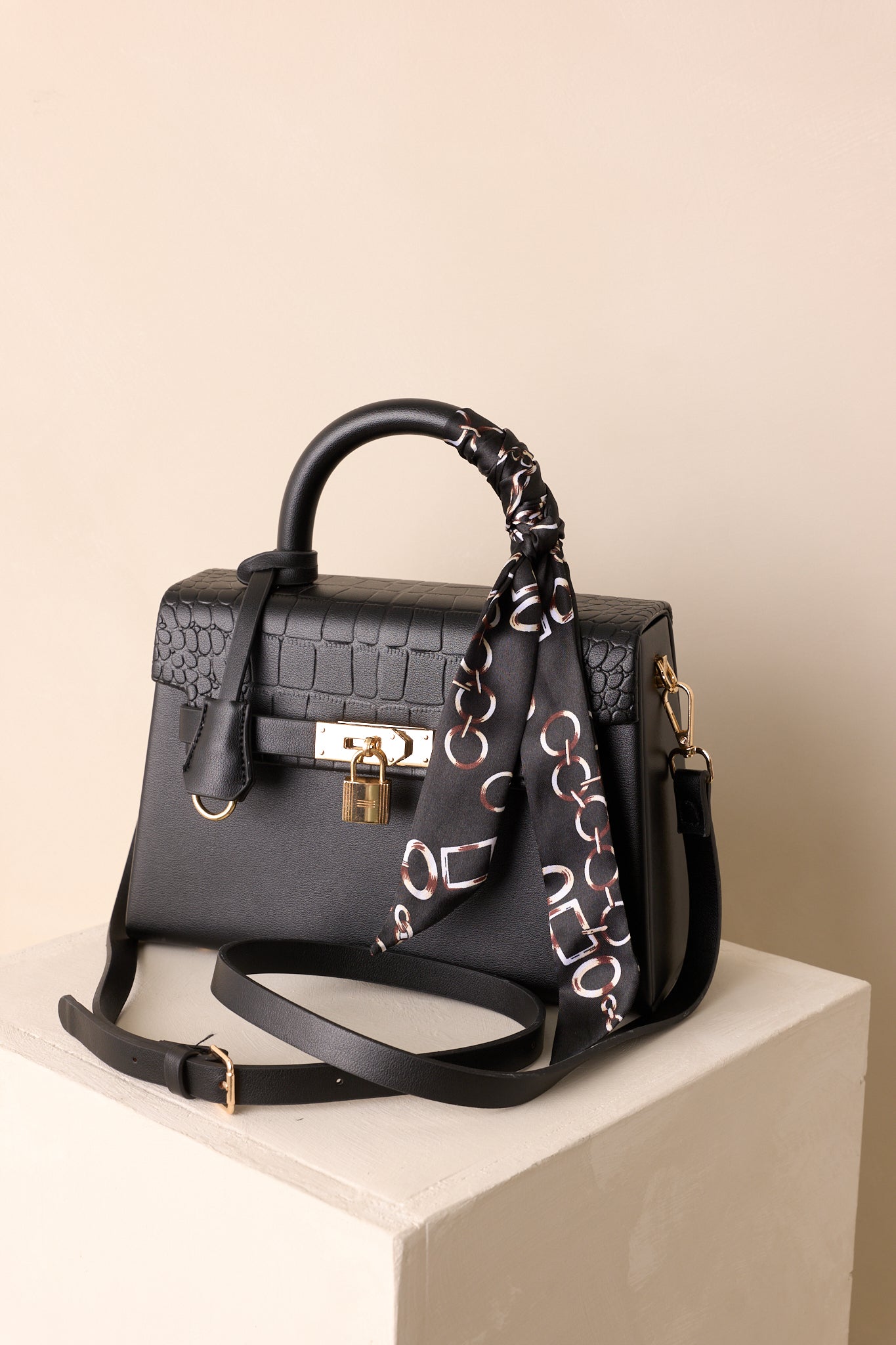 Cropped view focusing on the black handbag’s front flap, padlock closure, and smooth faux leather material.