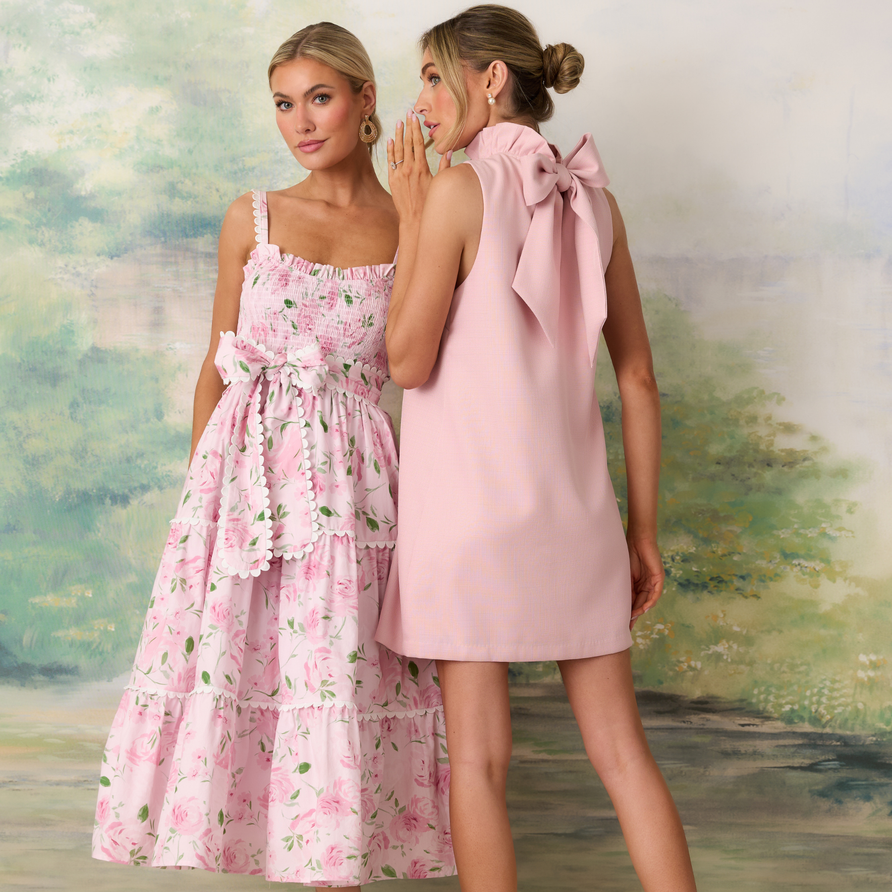 Two women wearing pink dresses standing in front of a scenic background.