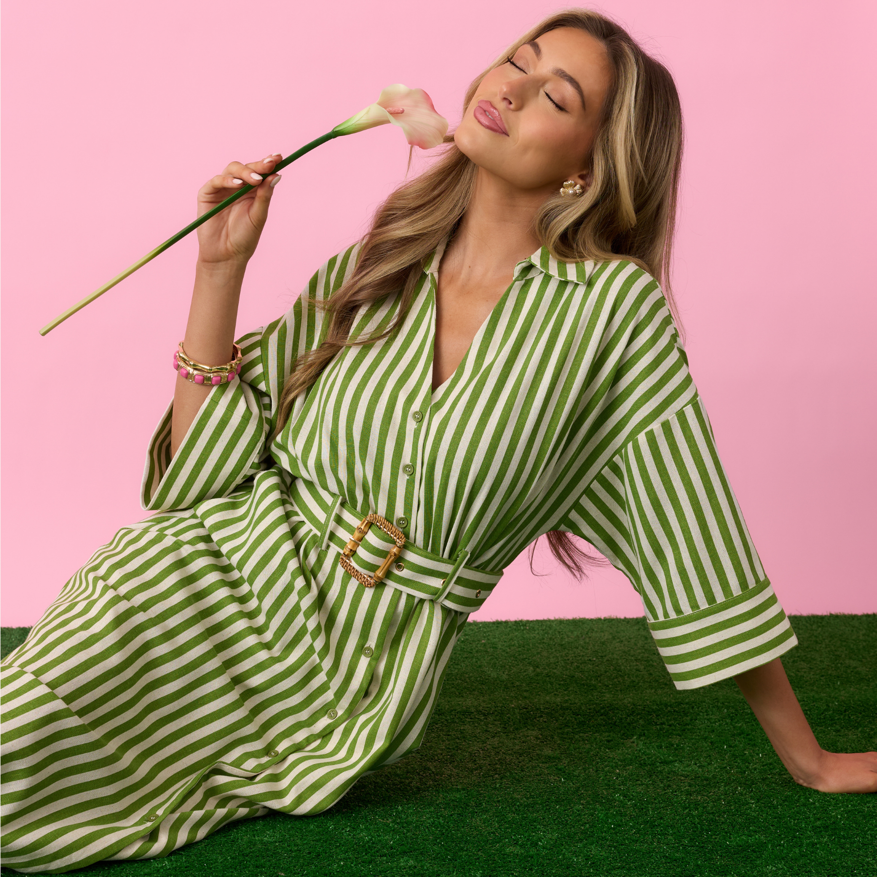 Woman in a green and white striped dress holding a flower against a pink background.