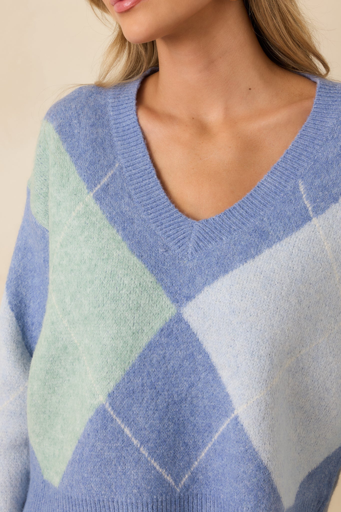 Close-up of the blue argyle sweater showing ribbed trim, V-neckline, and knit texture.