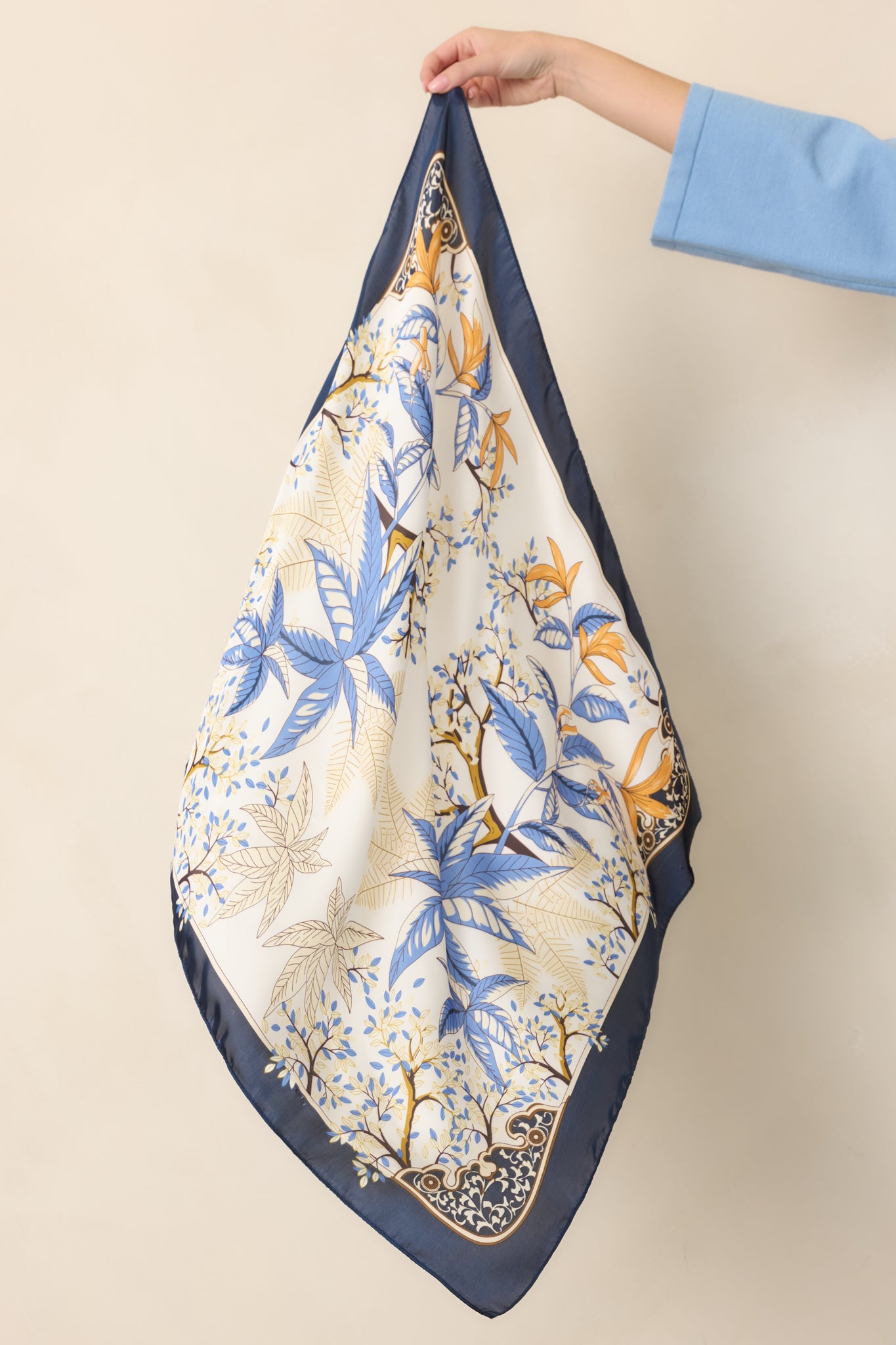 Decorative scarf showcasing a botanical print of blue foliage and golden flowers against a rich navy-bordered design.